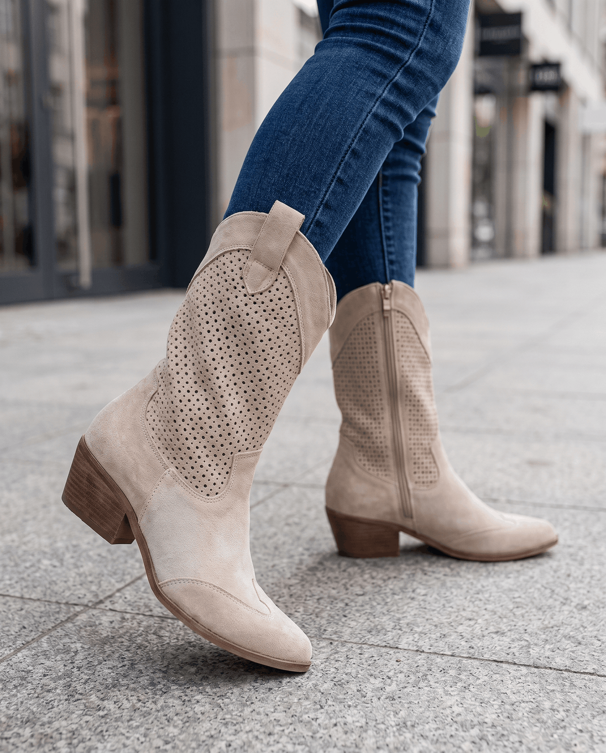 Beige perforated boots worn walking on a city sidewalk with tucked jeans