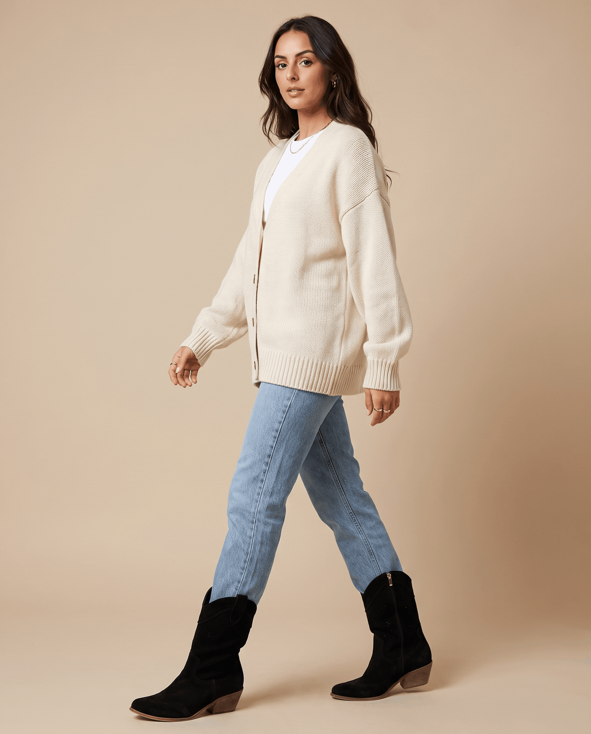 Woman in a cream sweater and light-wash jeans walking in black western boots