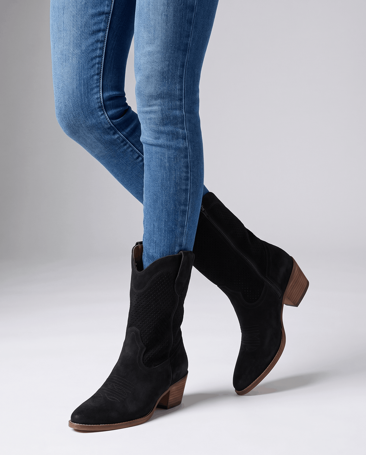 Black perforated boots worn standing with light-wash jeans tucked in