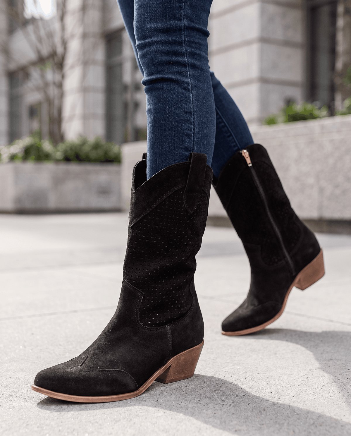 Black western boots worn walking on a city sidewalk with dark jeans