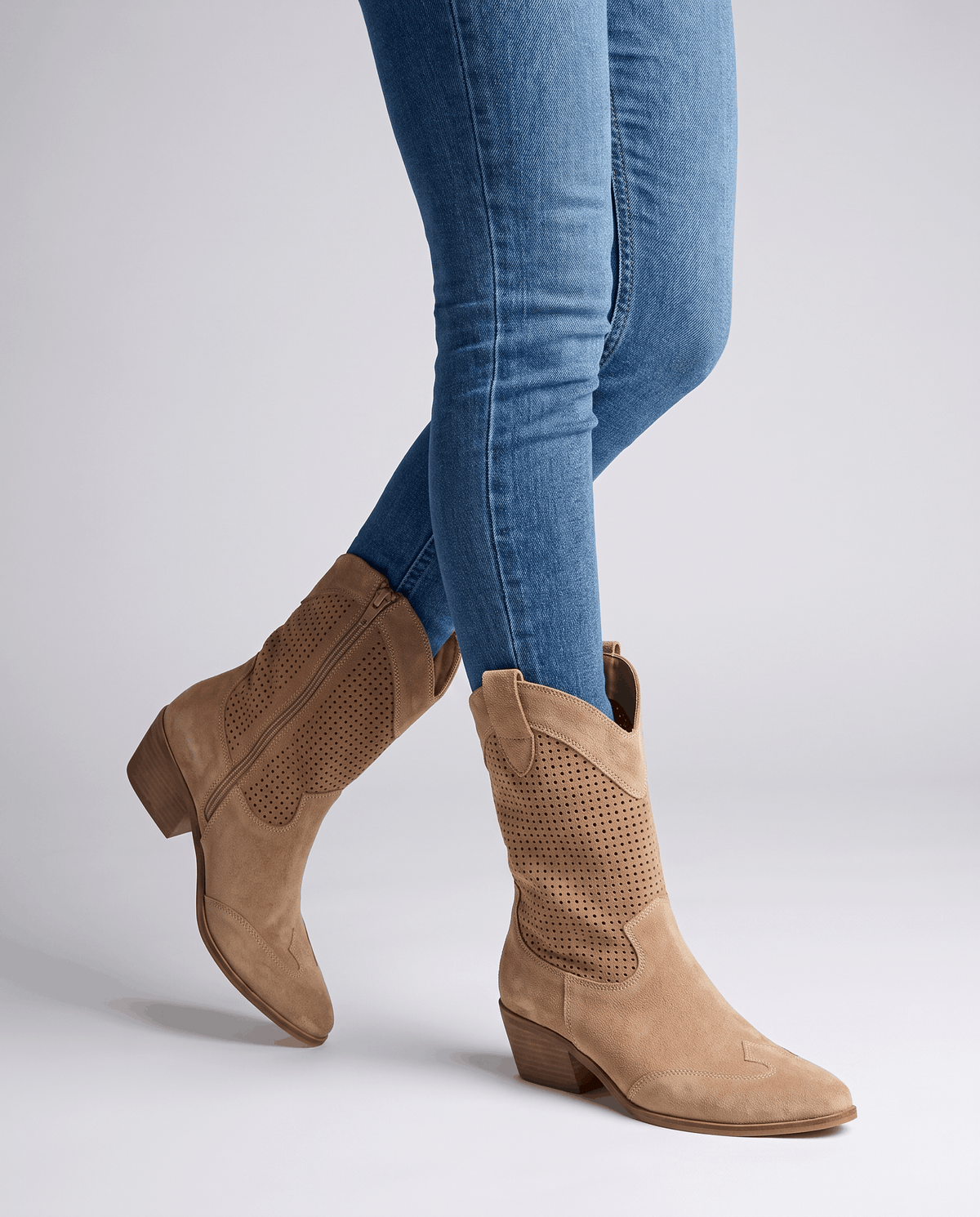 Brown perforated cowboy boots worn standing with blue skinny jeans tucked in