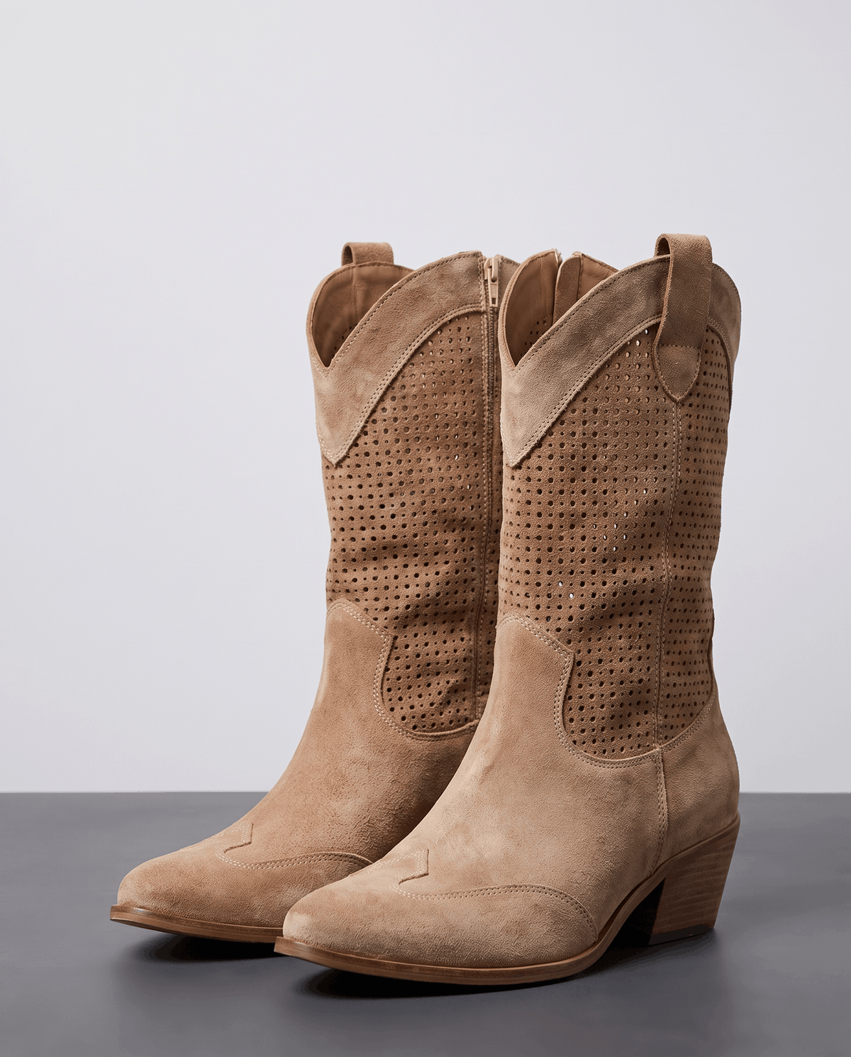 Pair of brown perforated western boots on a grey studio floor