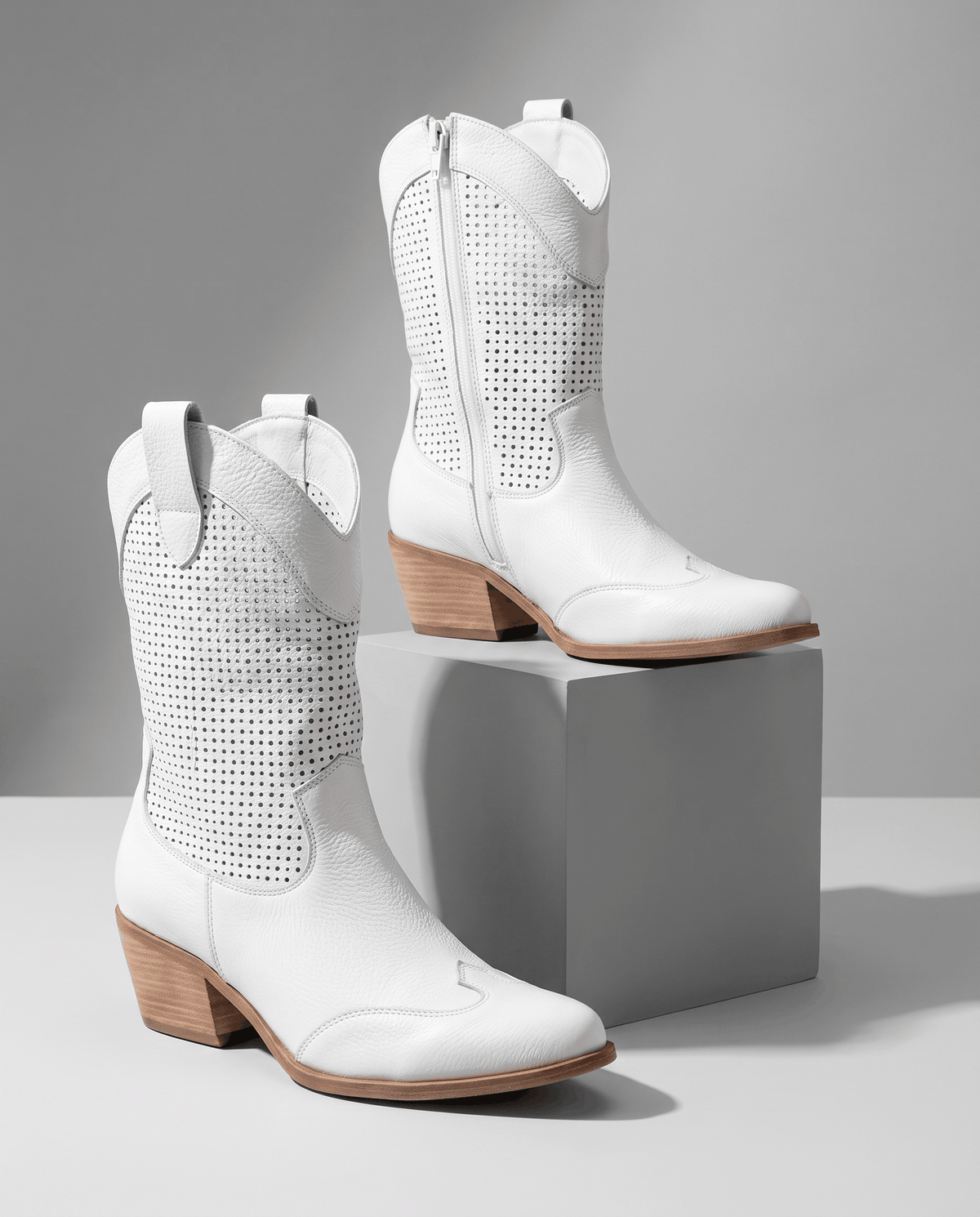 White perforated boots displayed on a grey pedestal