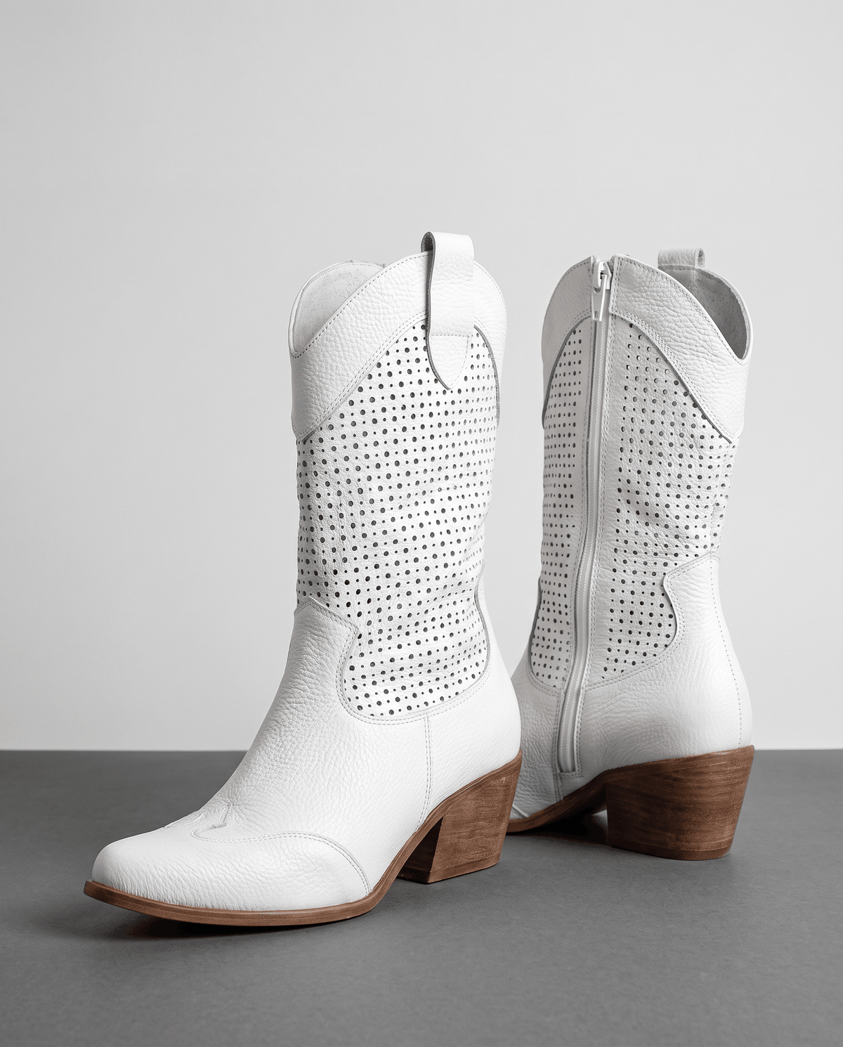 Pair of white perforated cowboy boots with pointed toes, inside zip and stacked heels