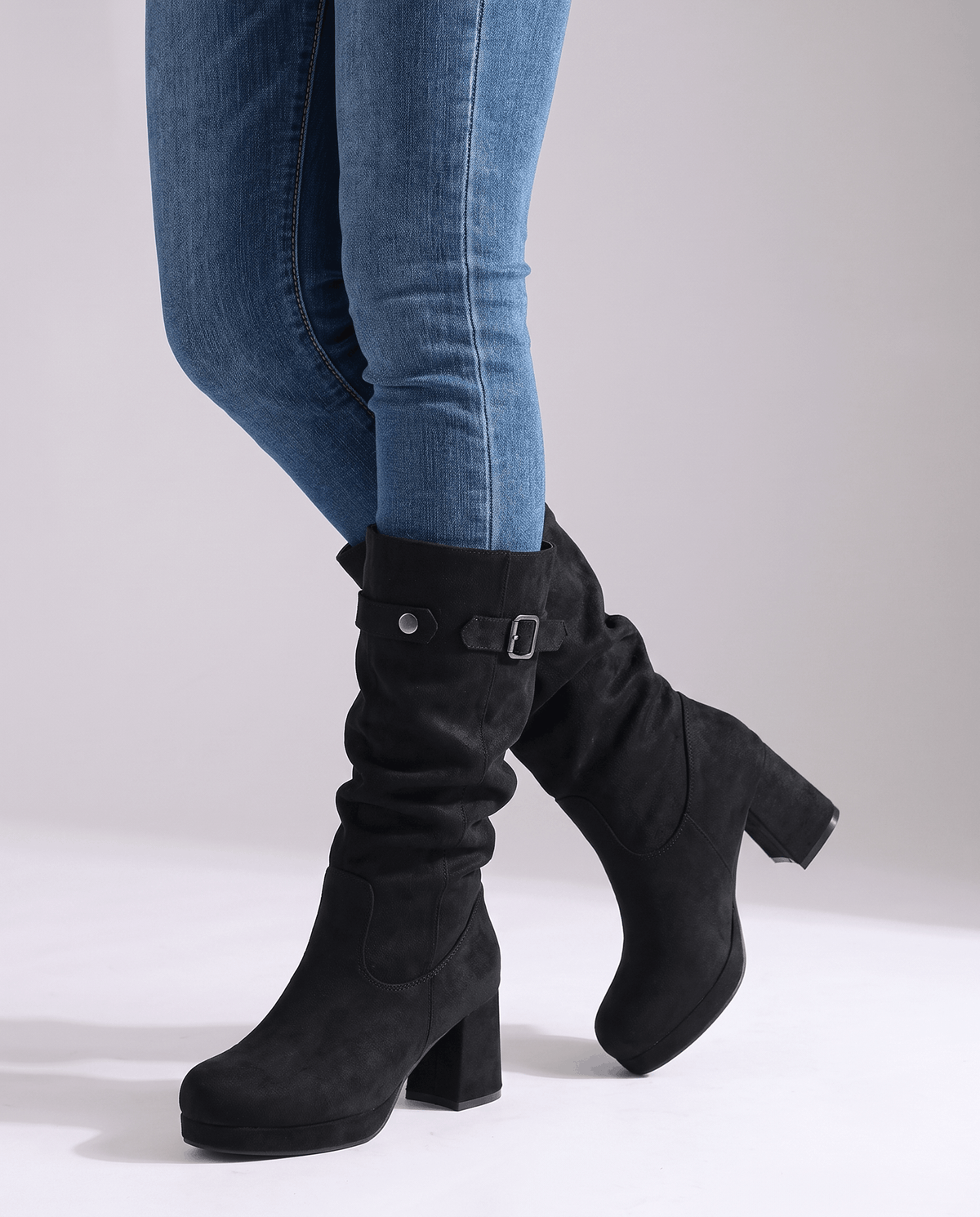 Woman in blue skinny jeans walking in black slouch boots on a white floor
