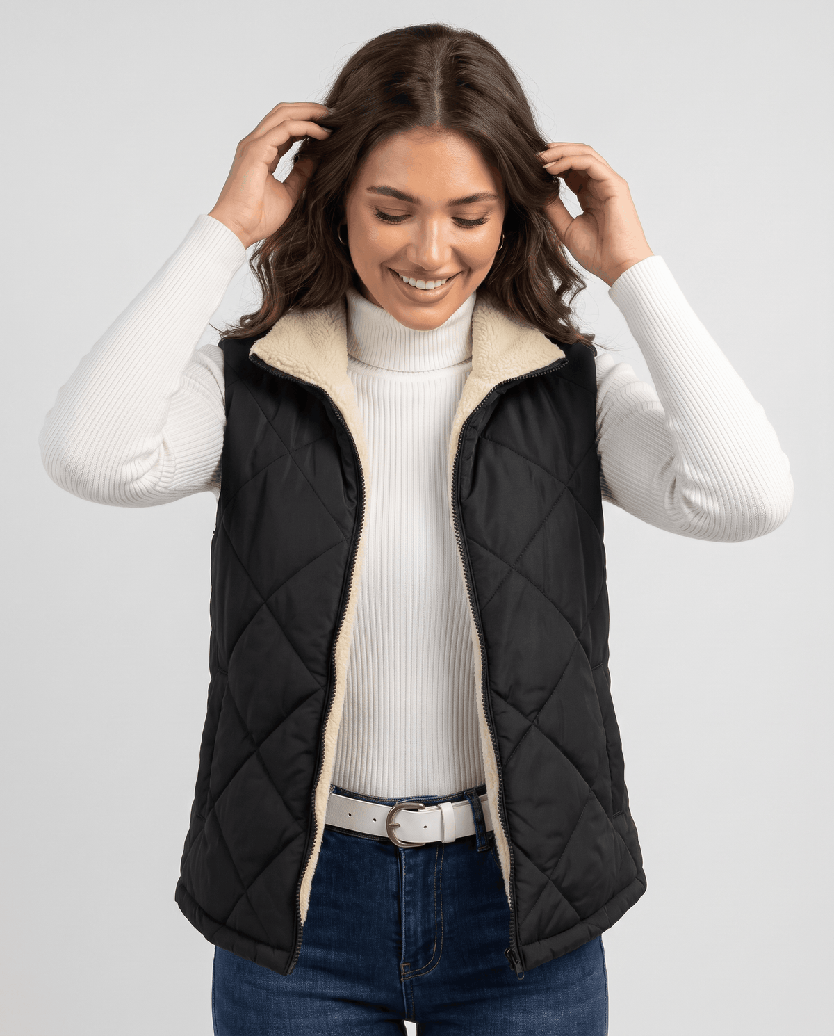 Black diamond-quilted vest worn over a white turtleneck with blue jeans