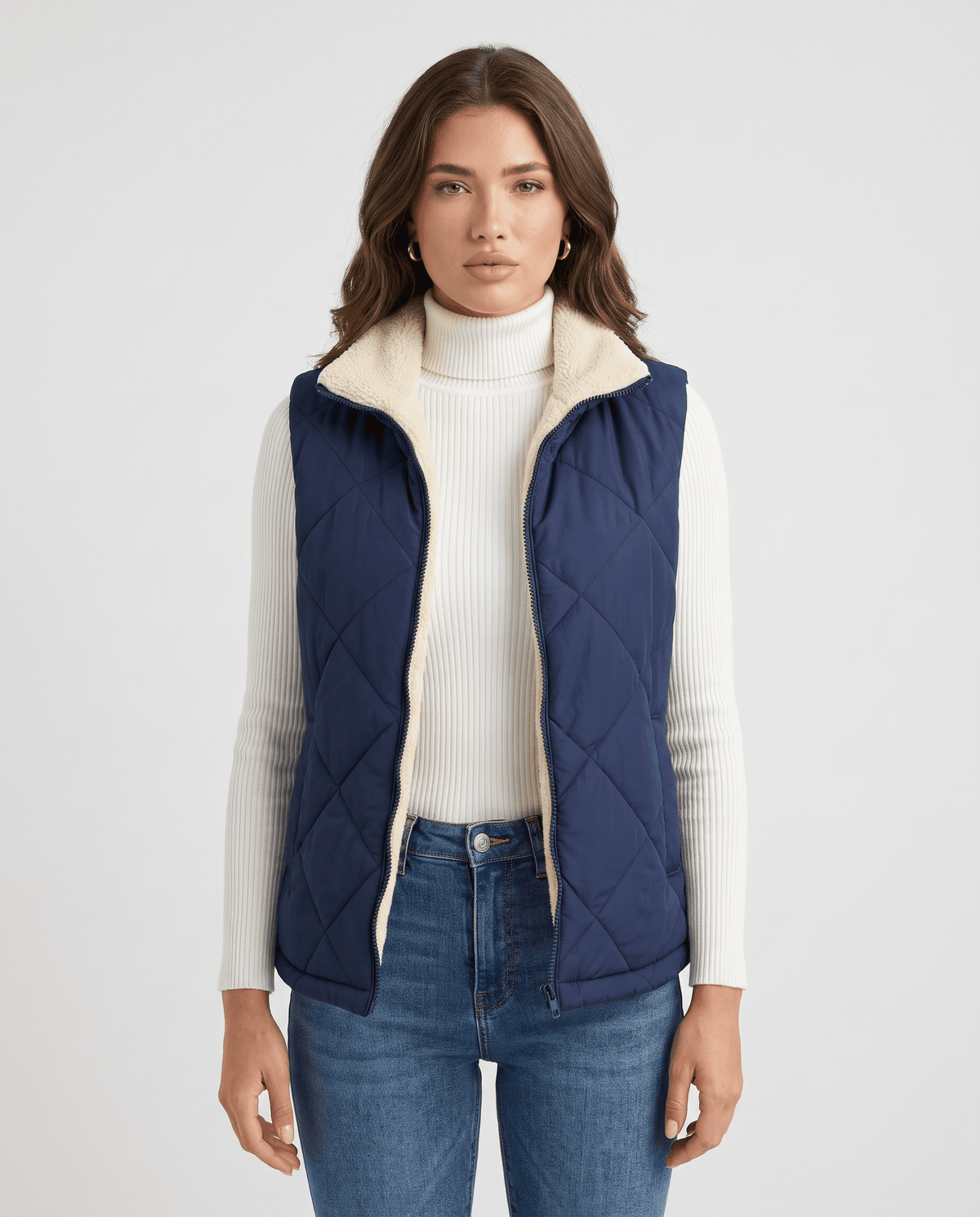 Women's quilted puffer vest in blue with stand collar worn over a white turtleneck