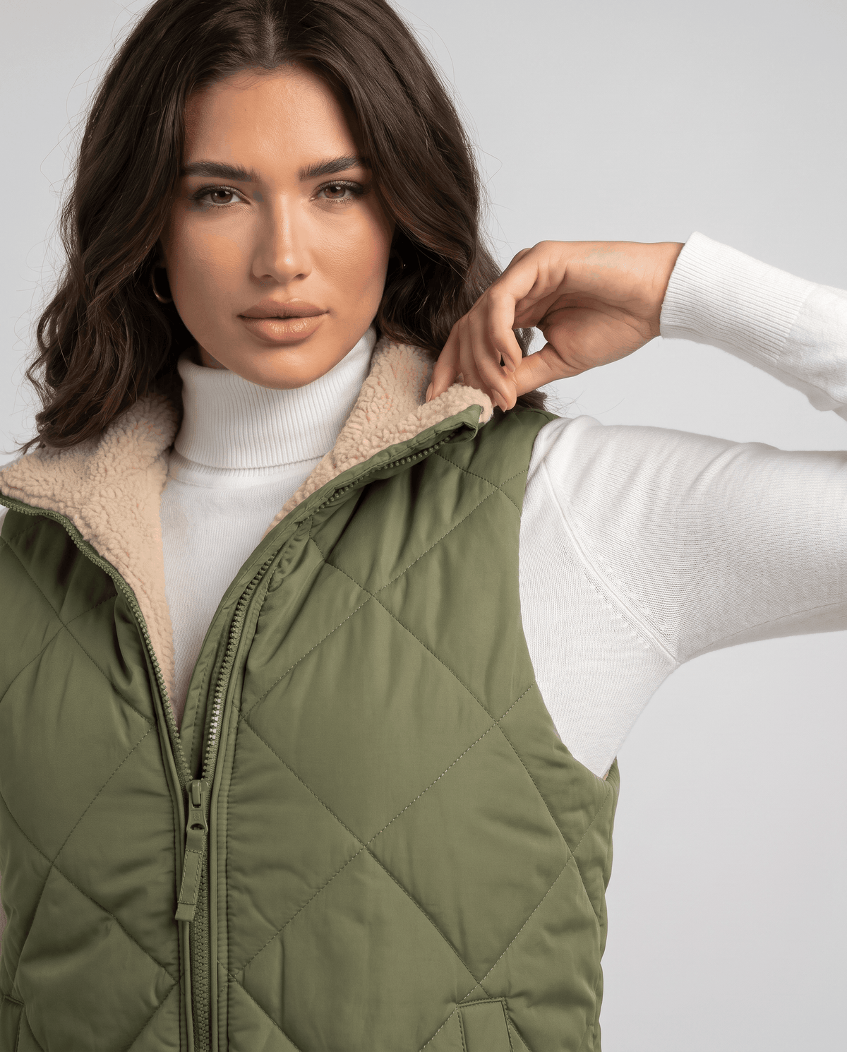 Model touching the stand collar of a green quilted vest