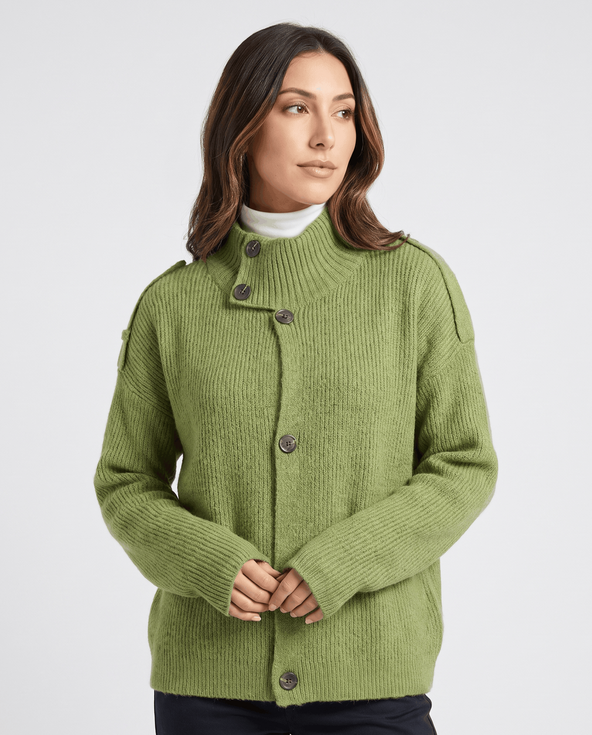 Woman wearing green ribbed knit cardigan with stand collar and button front over a white turtleneck