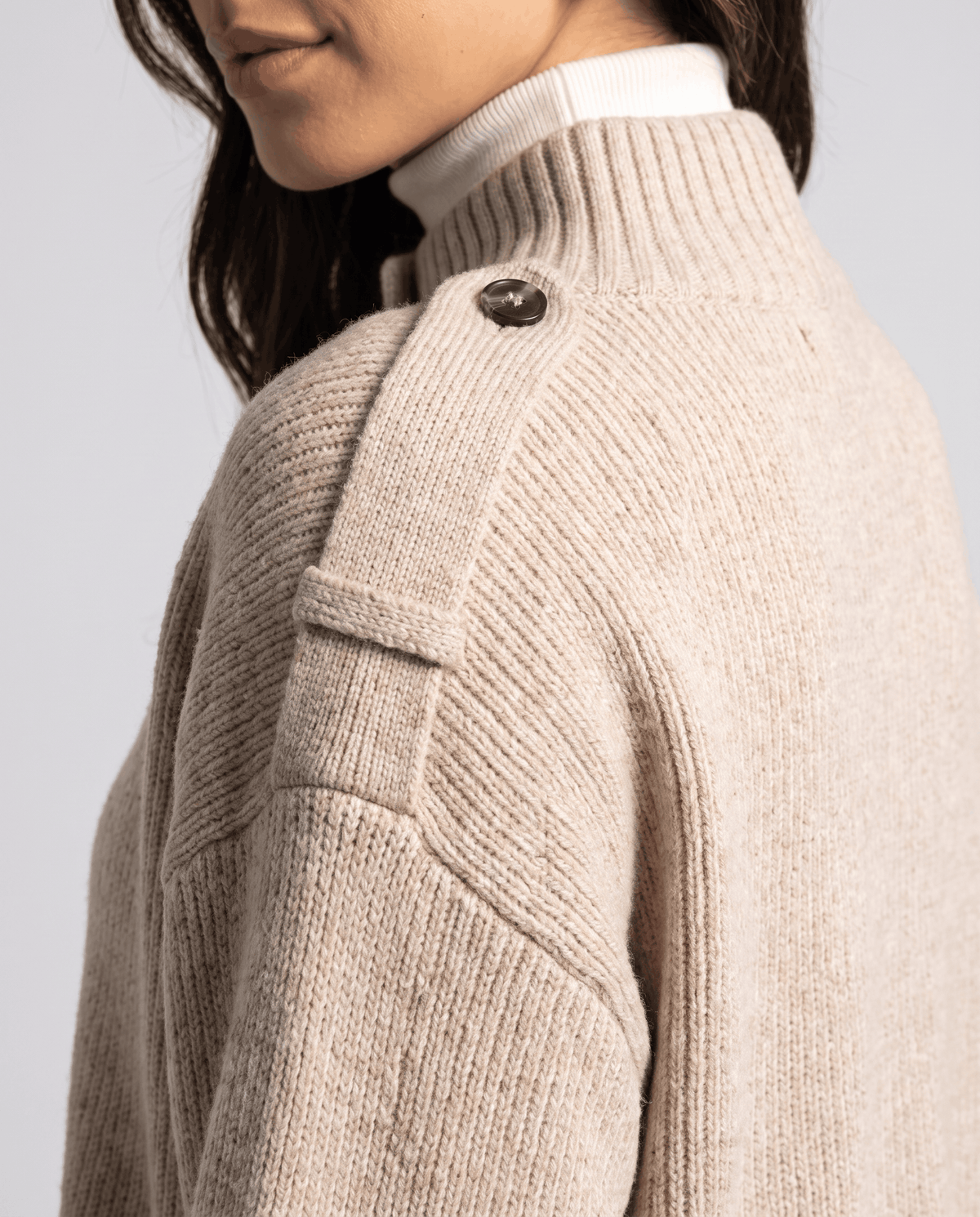 Close-up of light beige ribbed cardigan shoulder strap button and stand collar detail