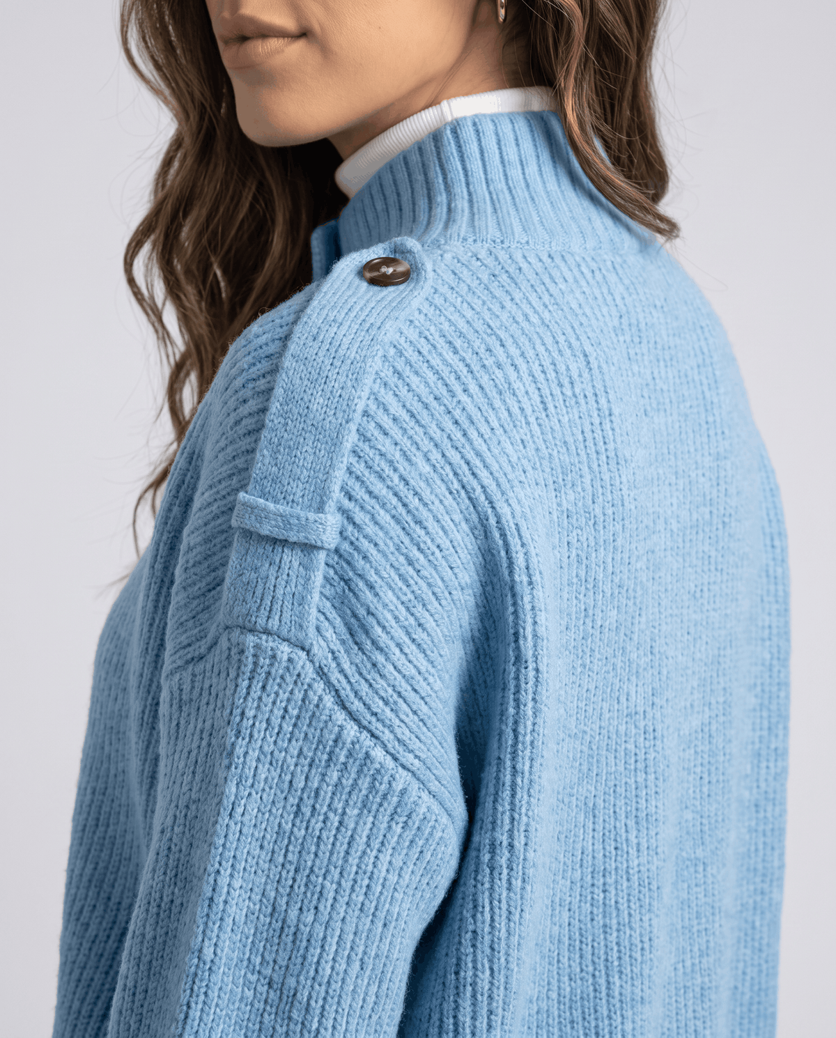 Close-up of sky blue ribbed cardigan shoulder strap button and stand collar detail
