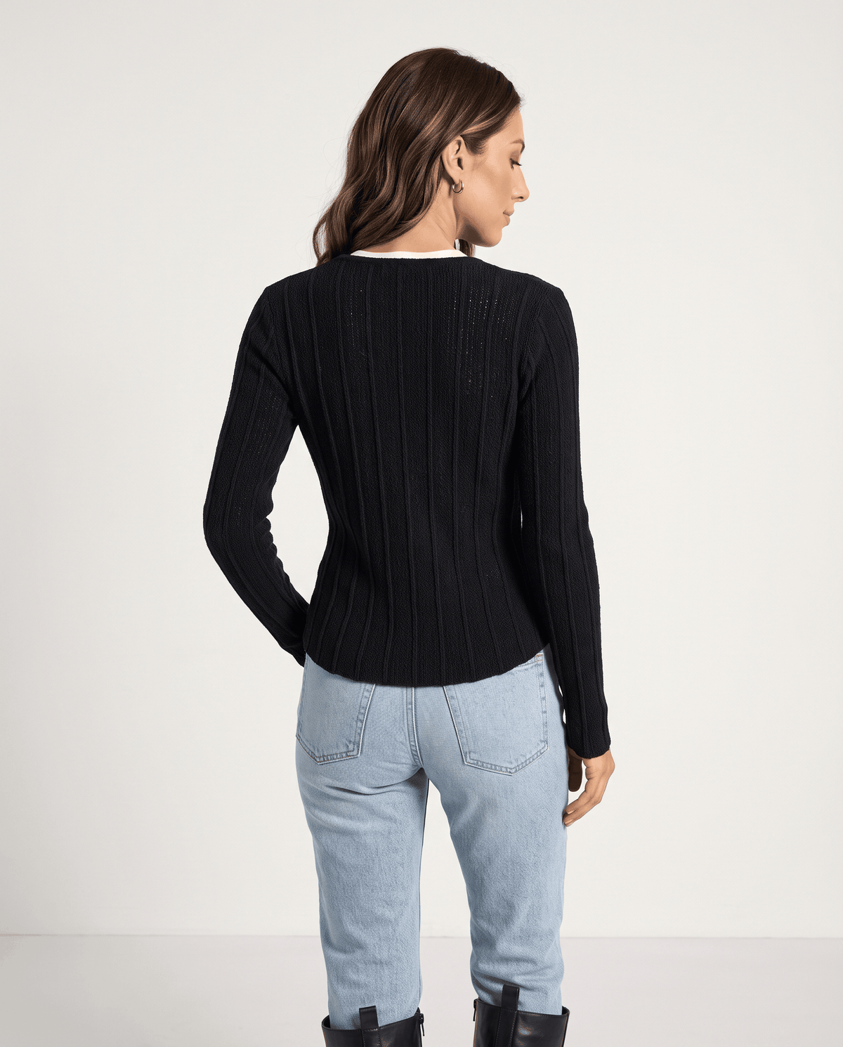 Back view of black ribbed cardigan worn with light blue jeans and boots