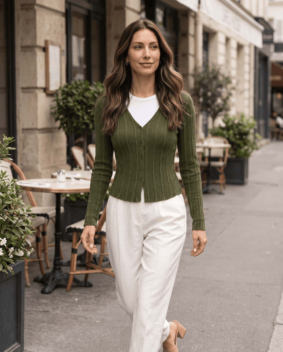 Woman walking in a green ribbed button-front cardigan and cream trousers outside a café