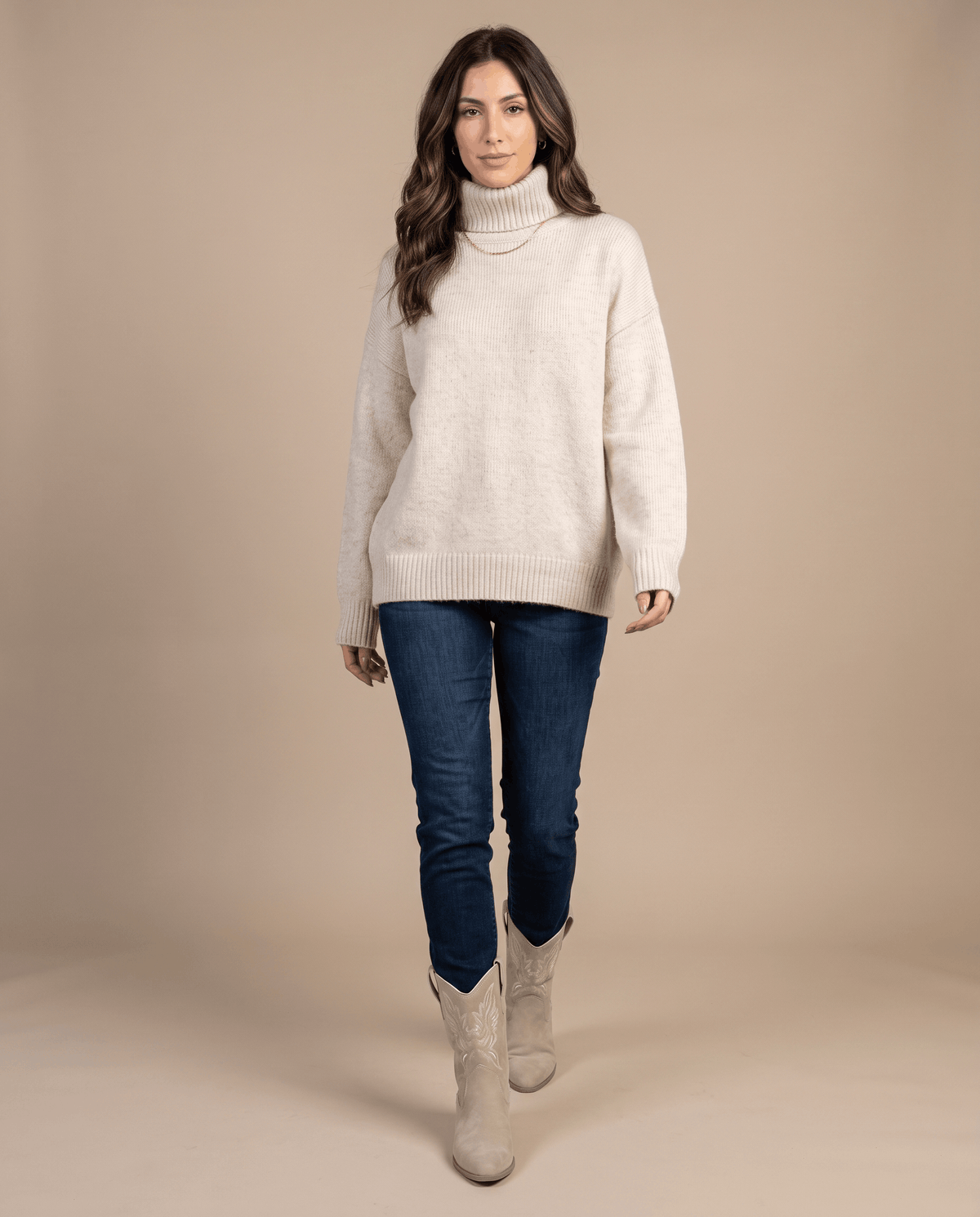 Woman in a cream turtleneck sweater and blue jeans wearing beige boots