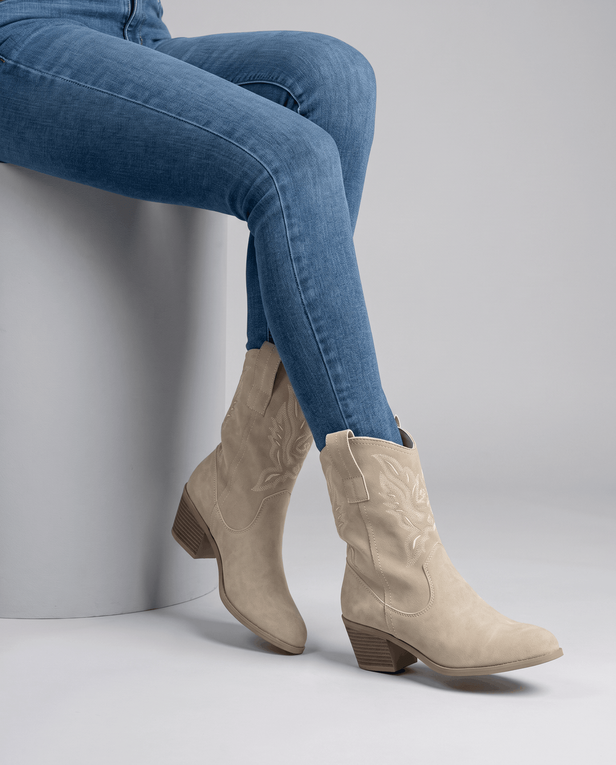 Seated model with legs crossed in beige boots and tucked blue jeans