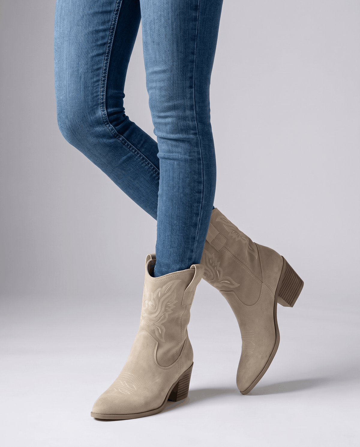 Beige western boots worn standing with skinny jeans tucked into the shaft