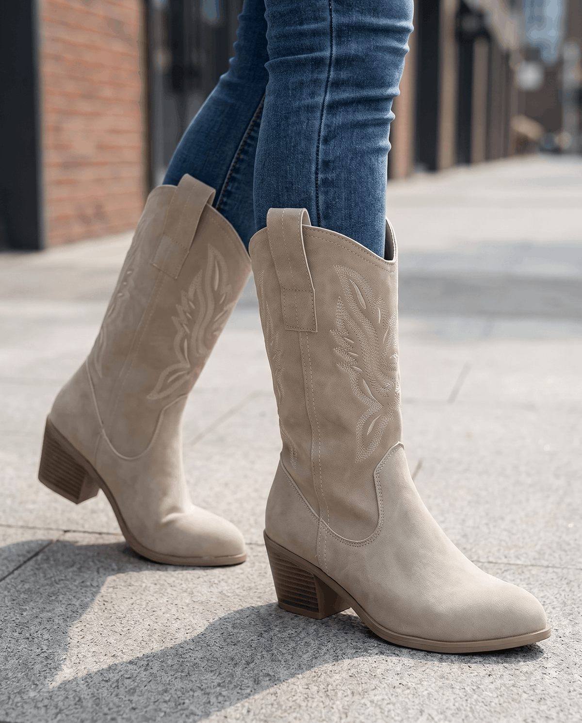 Beige embroidered boots mid-stride on a sunny city sidewalk with blue jeans