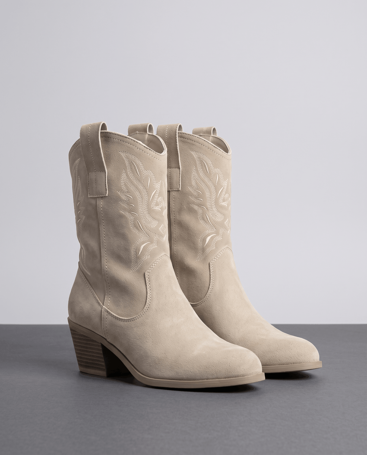 Pair of beige embroidered boots with stacked heels on a grey studio floor