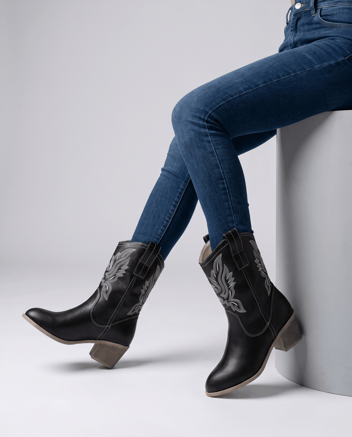 Seated model with dark jeans tucked into black embroidered western boots