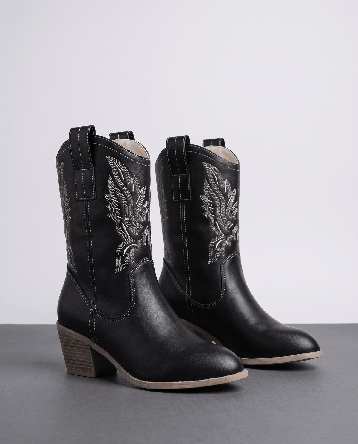 Pair of black western boots with contrast grey embroidery on a studio floor