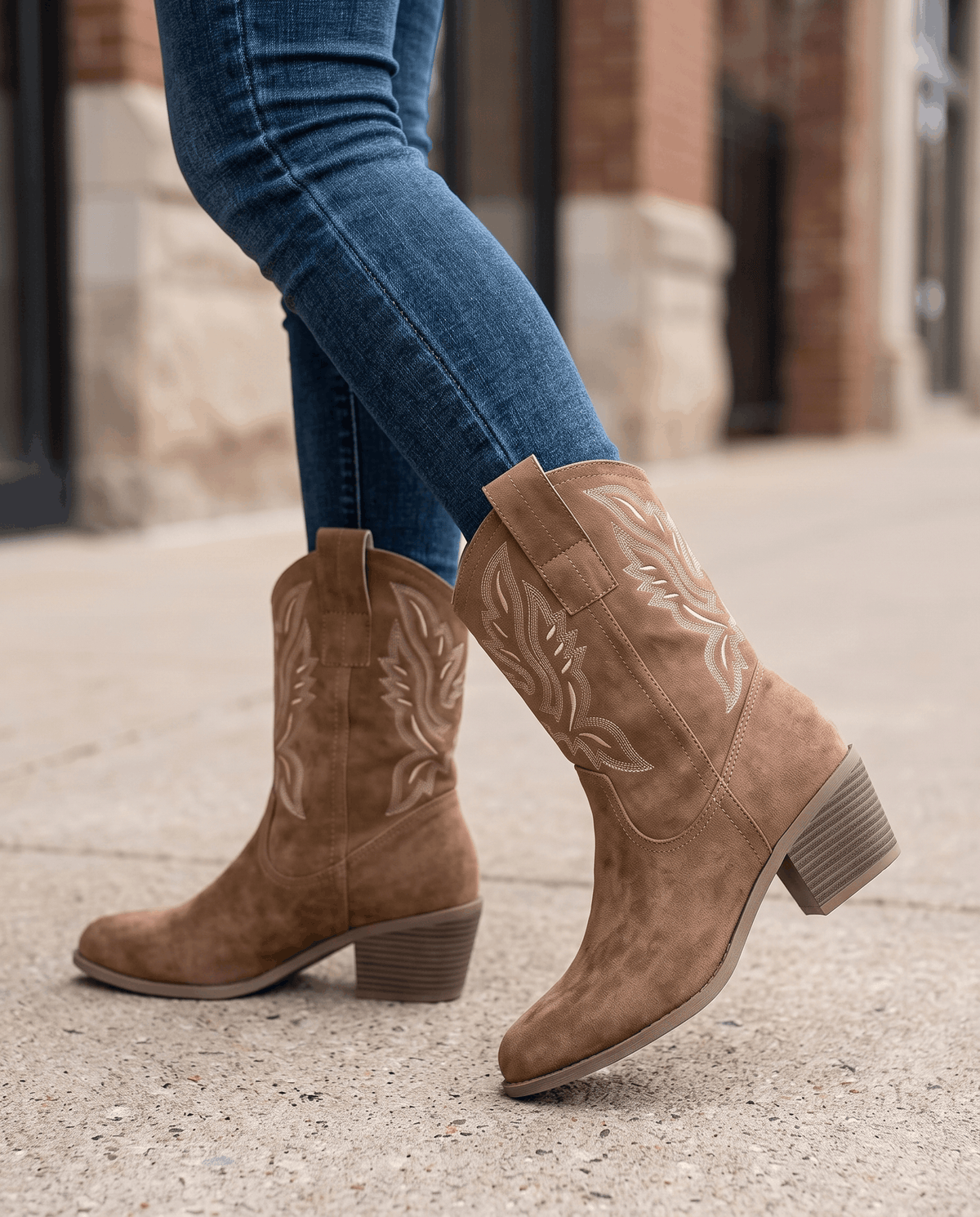 Camel boots worn walking on a city sidewalk with tucked blue jeans