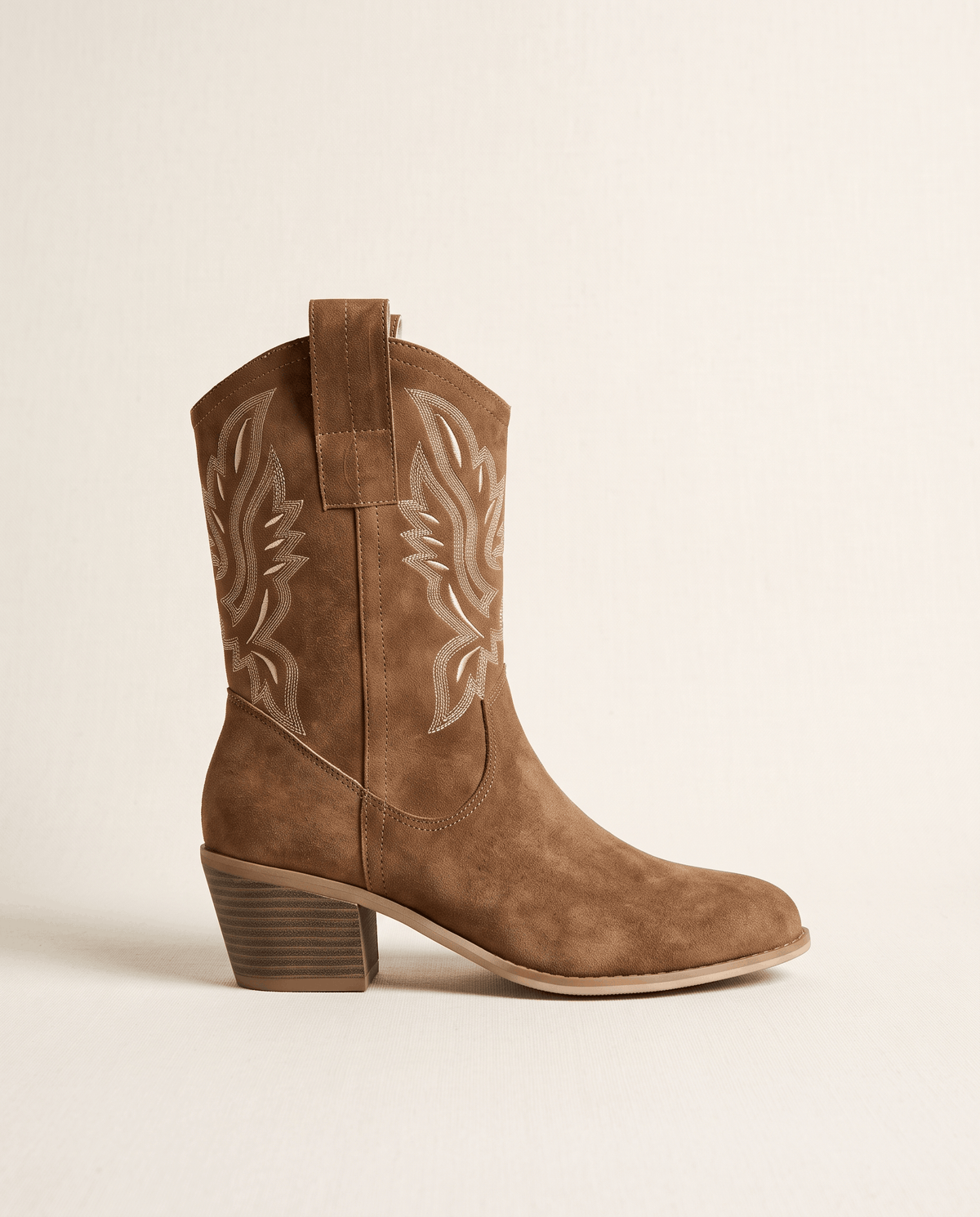 Single camel western boot in side profile against a soft cream backdrop