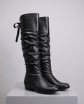 Black pair on a white display block showing the ruched shaft and round toe