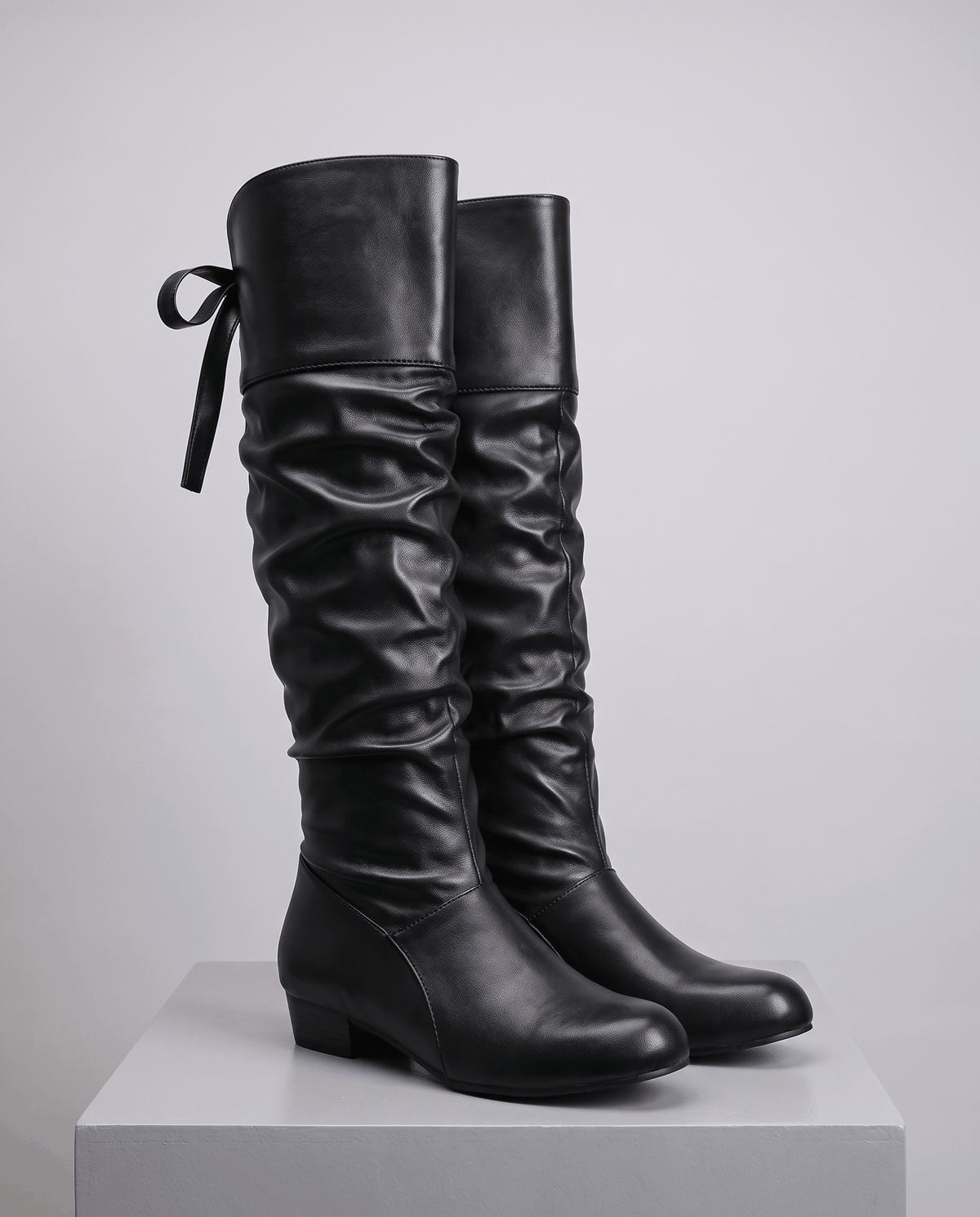 Black pair on a white display block showing the ruched shaft and round toe