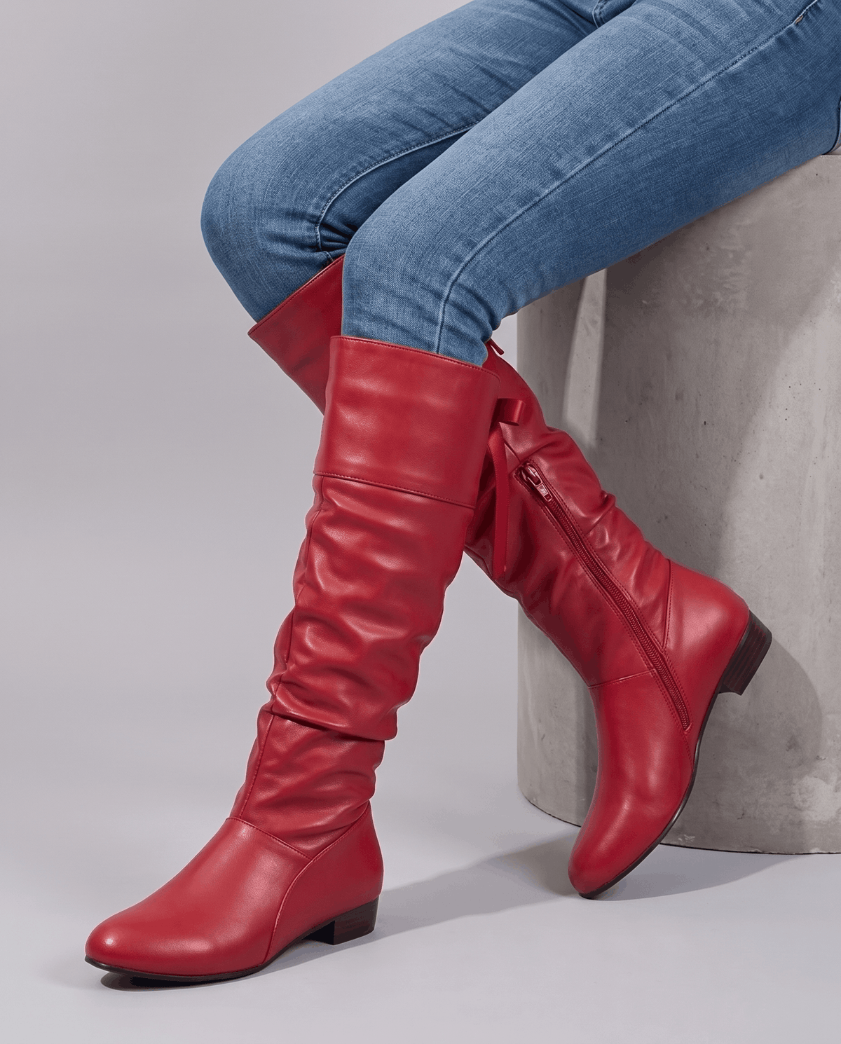 Seated woman in jeans wearing red boots with the inside zip visible