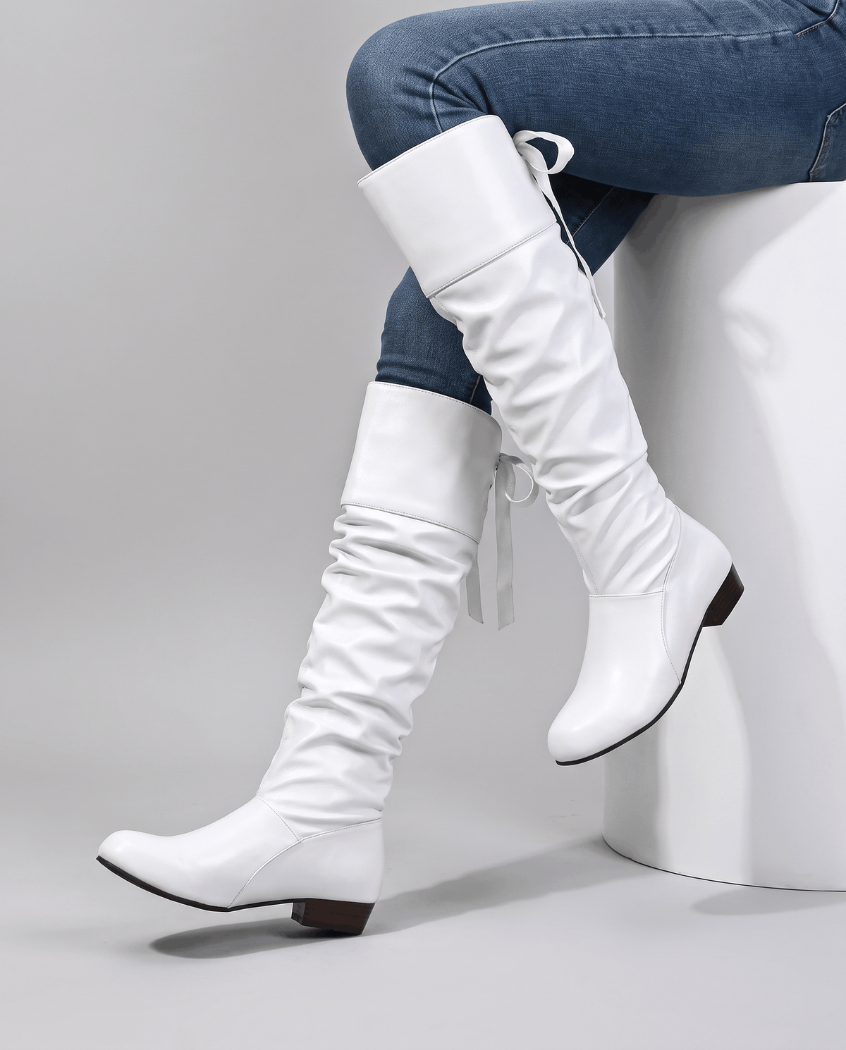 Seated woman in jeans wearing white knee-high boots on a white stool
