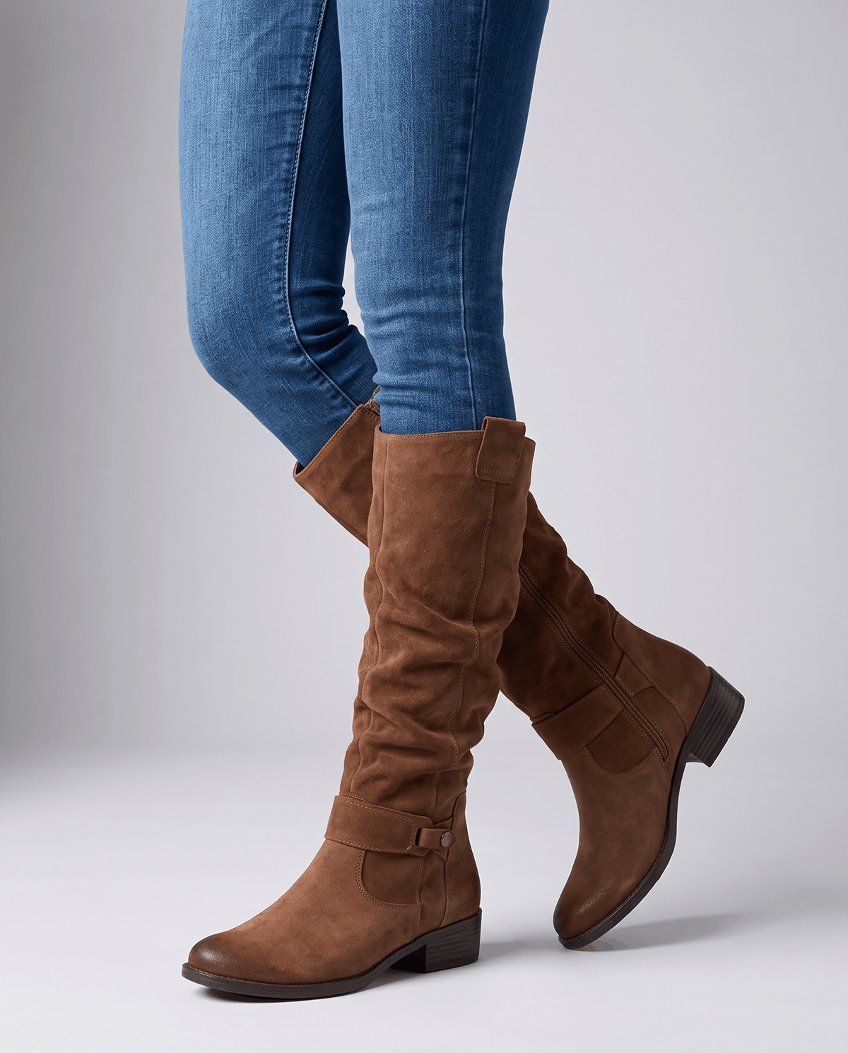 Woman in skinny blue jeans walking in brown slouchy boots with a low stacked heel