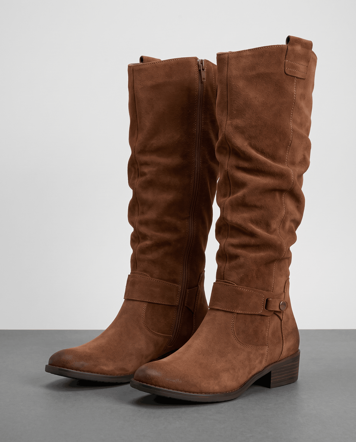 Pair of brown boots on a gray floor showing the inside zip and ankle buckle strap
