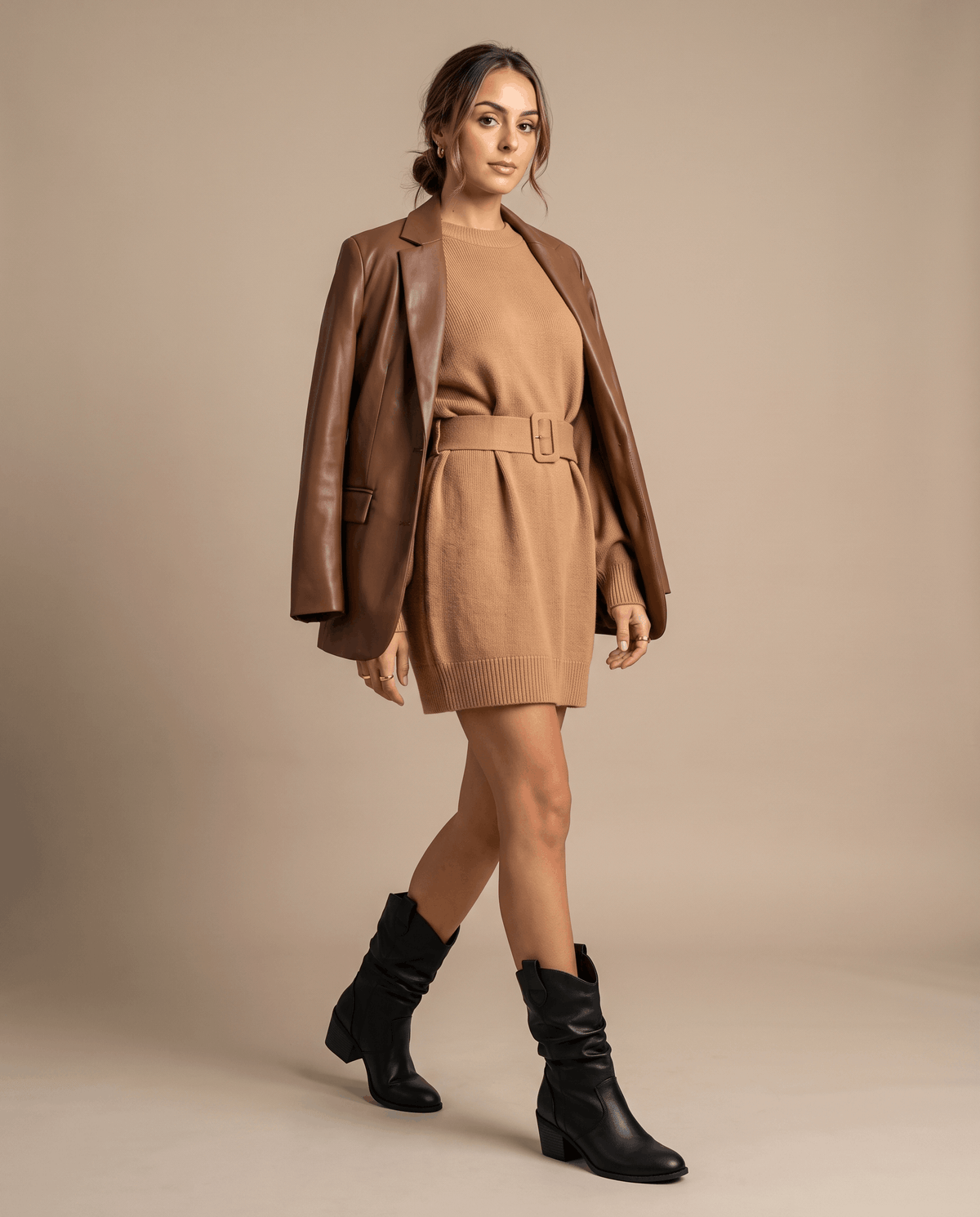 Woman in a camel blazer and sweater dress walking in black western boots