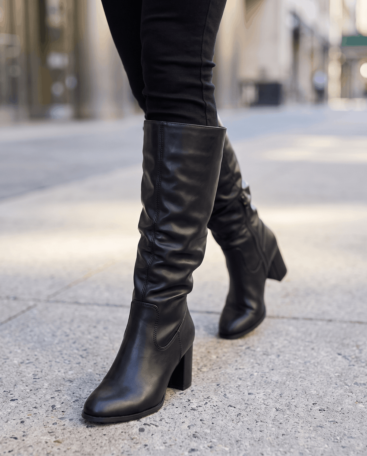 Black slouchy boots worn walking on a city sidewalk with black skinny jeans