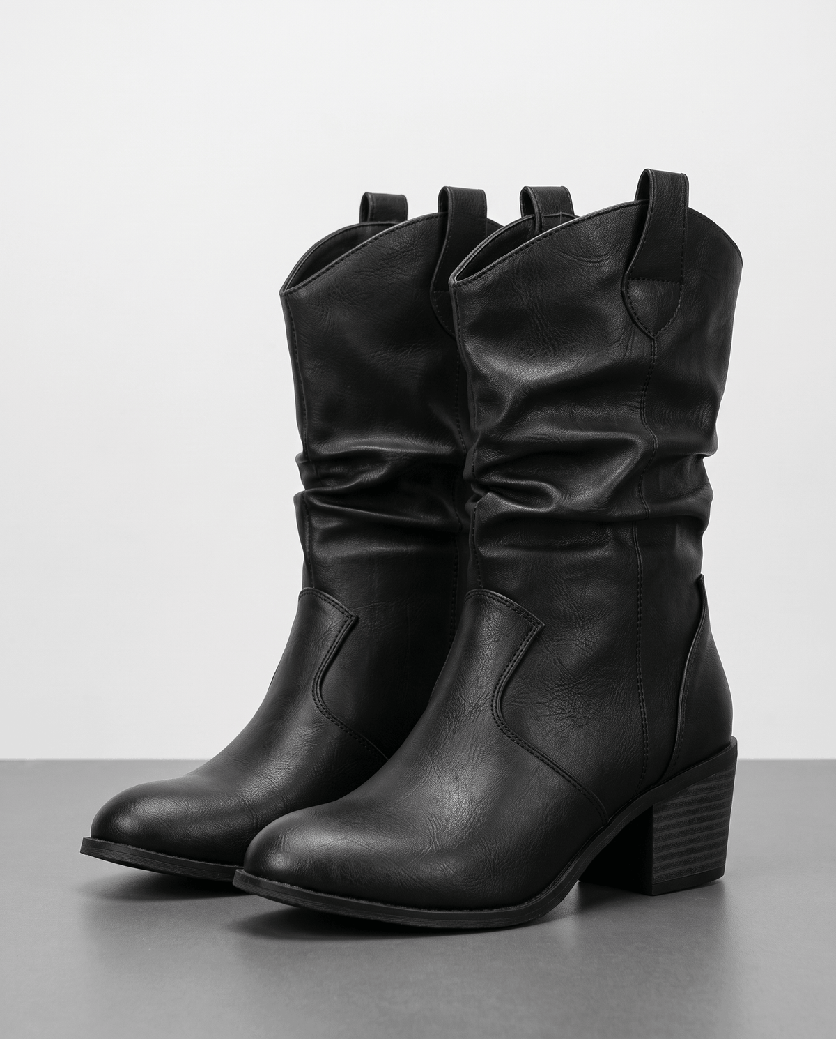 Pair of black slouchy western boots with pull tabs on a grey studio floor