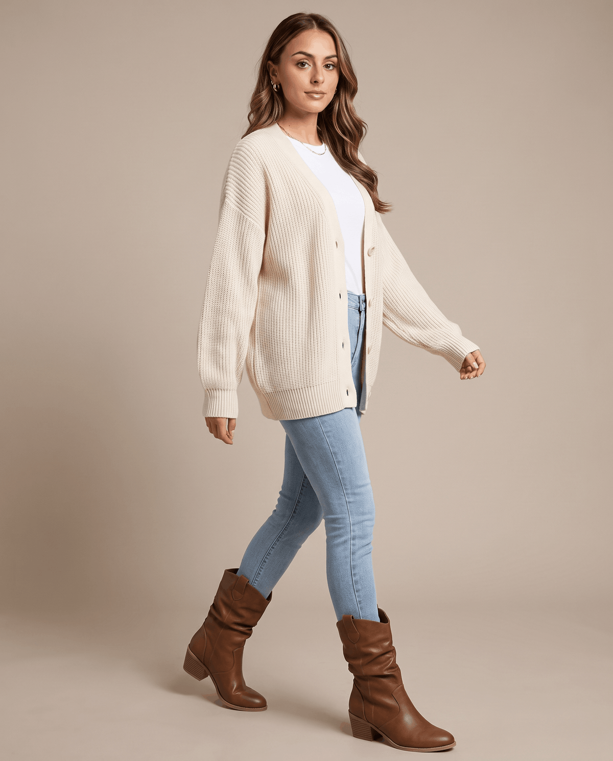 Woman in a cream cardigan and light-wash jeans walking in brown slouchy boots