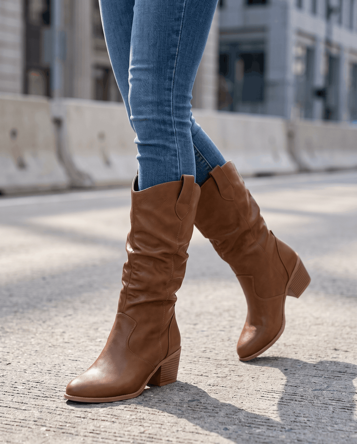 Brown western boots worn walking on a city street with tucked blue jeans