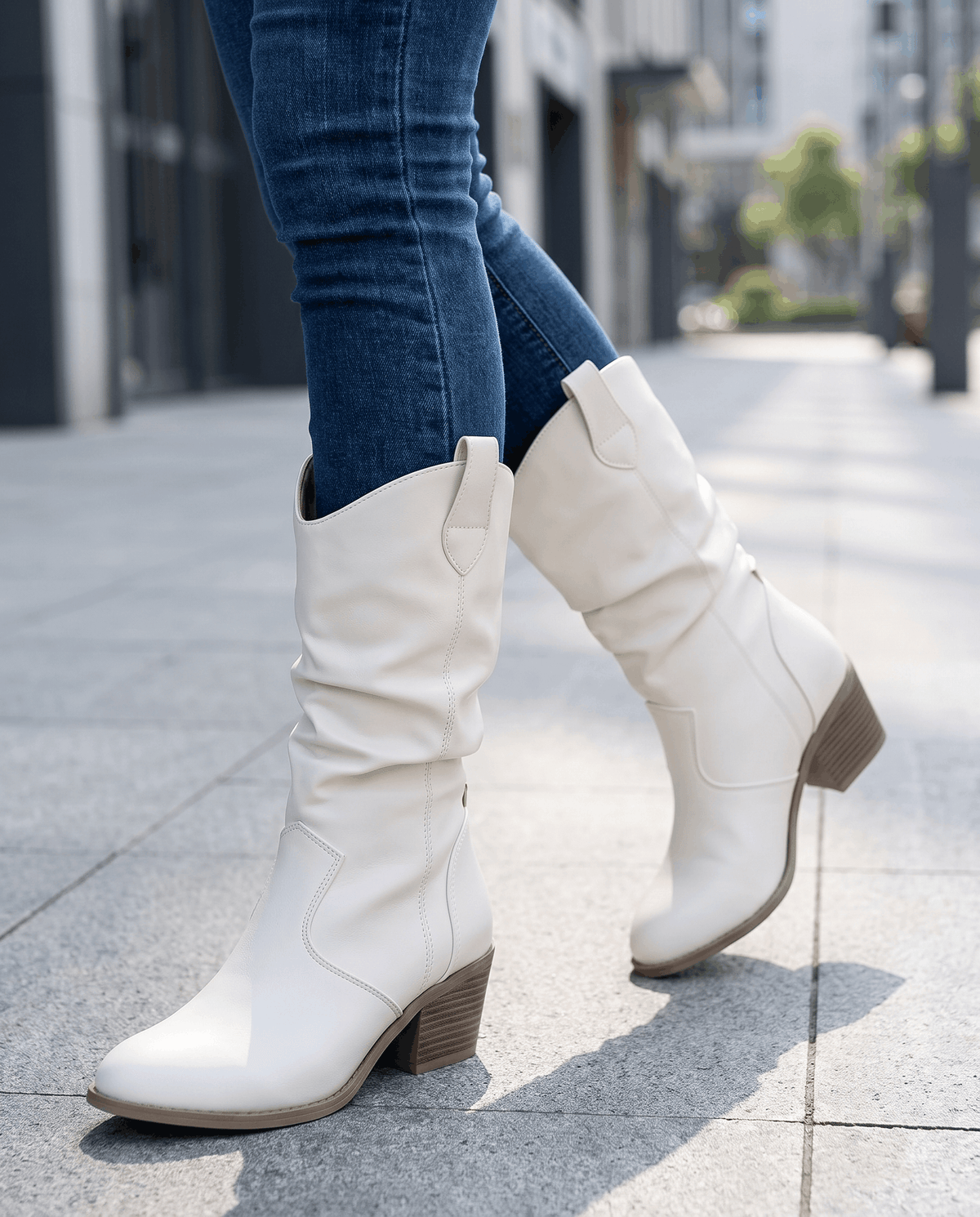 White slouchy boots mid-stride on a sunny sidewalk with blue jeans tucked in