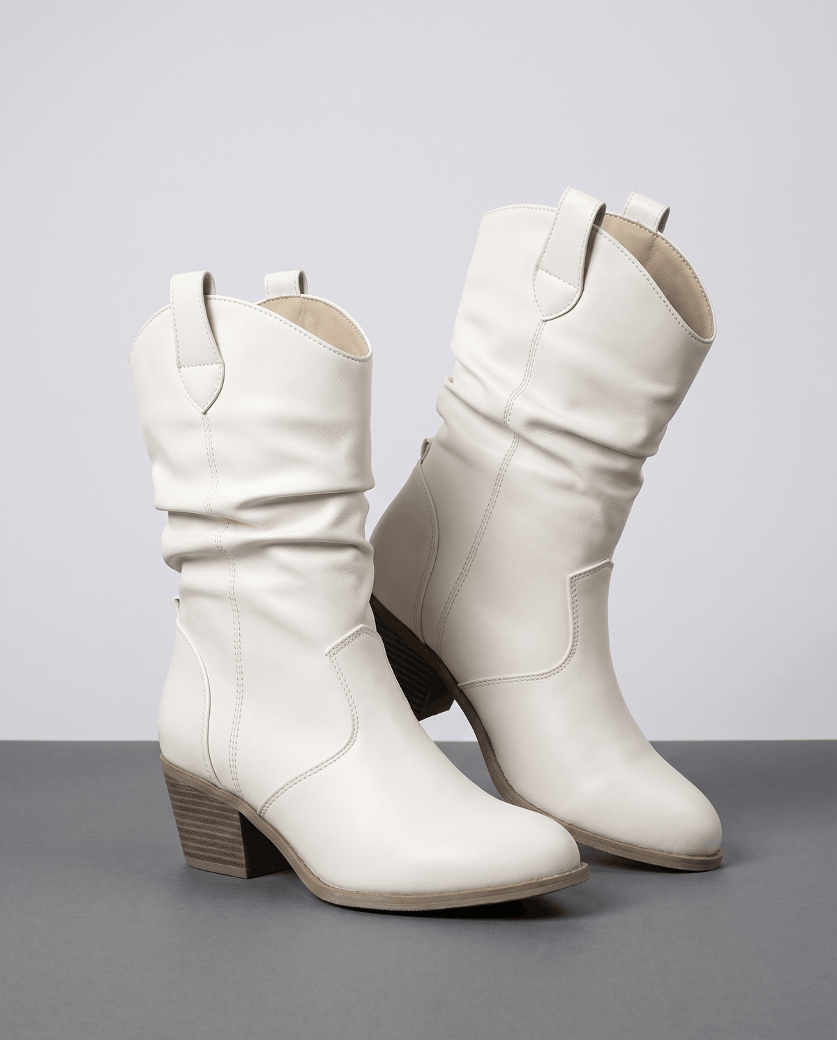 Pair of white slouchy cowboy boots with stacked heels on a grey studio floor