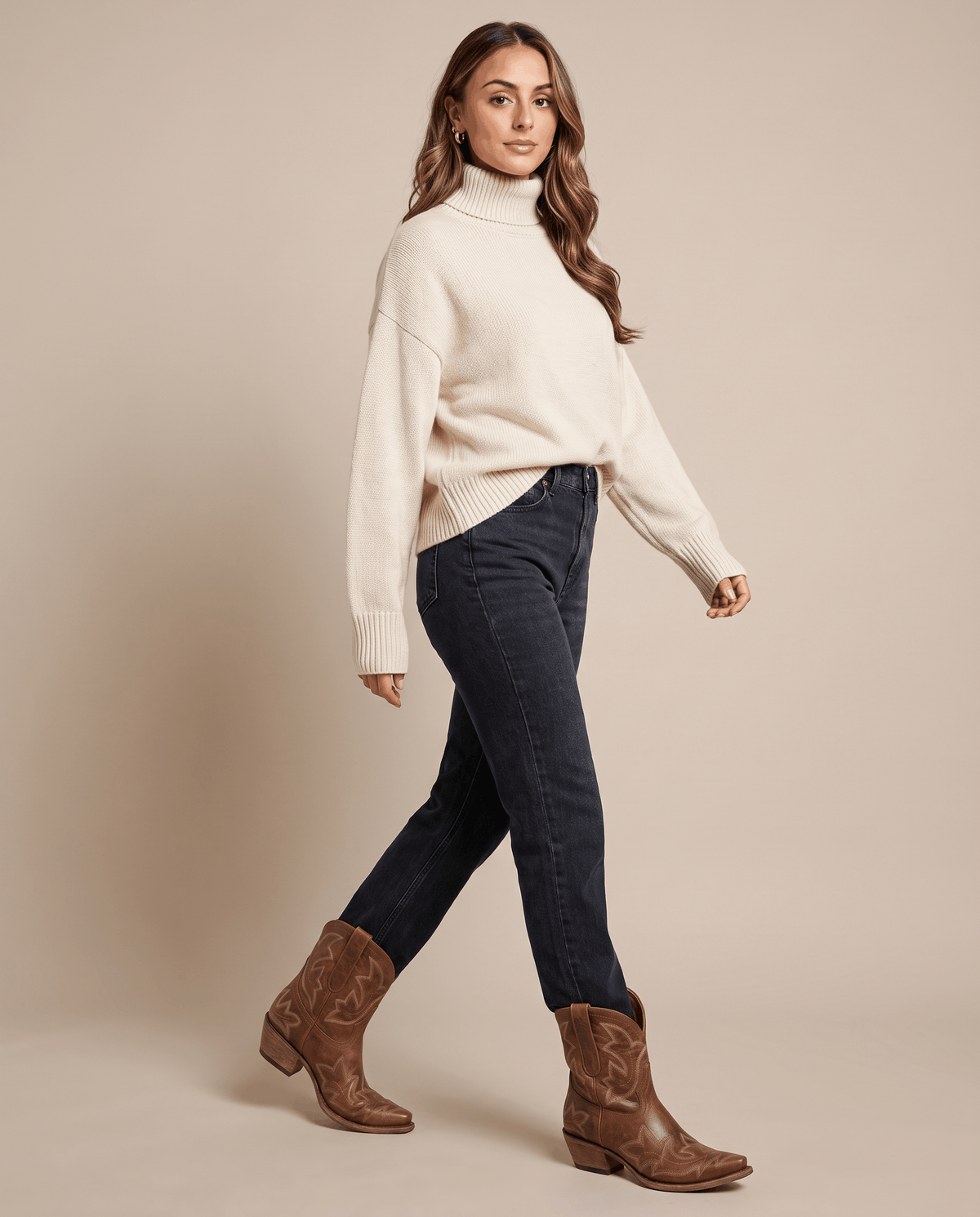 Woman in a cream turtleneck and dark jeans walking in brown cowboy boots