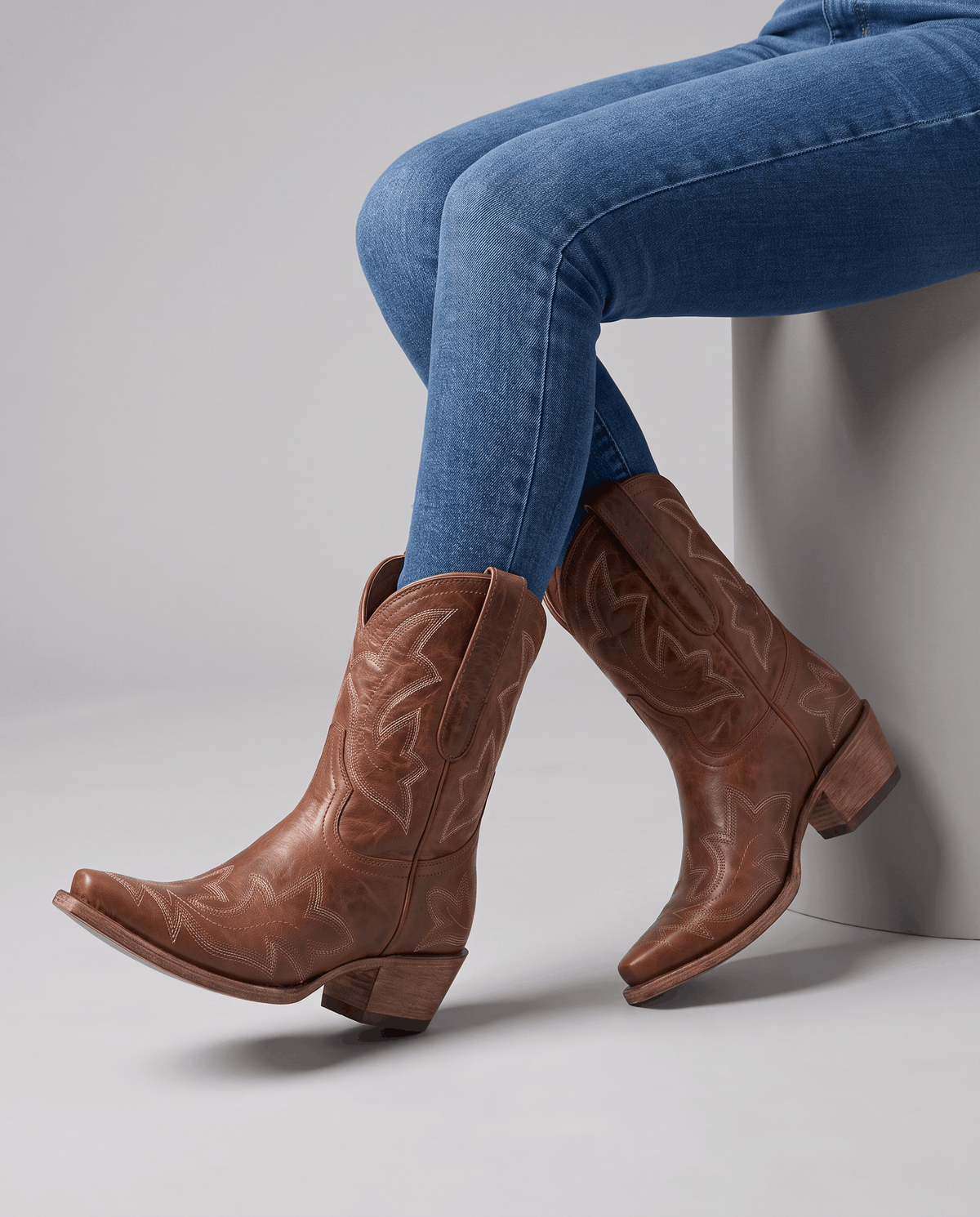 Seated model with blue jeans tucked into brown short western boots