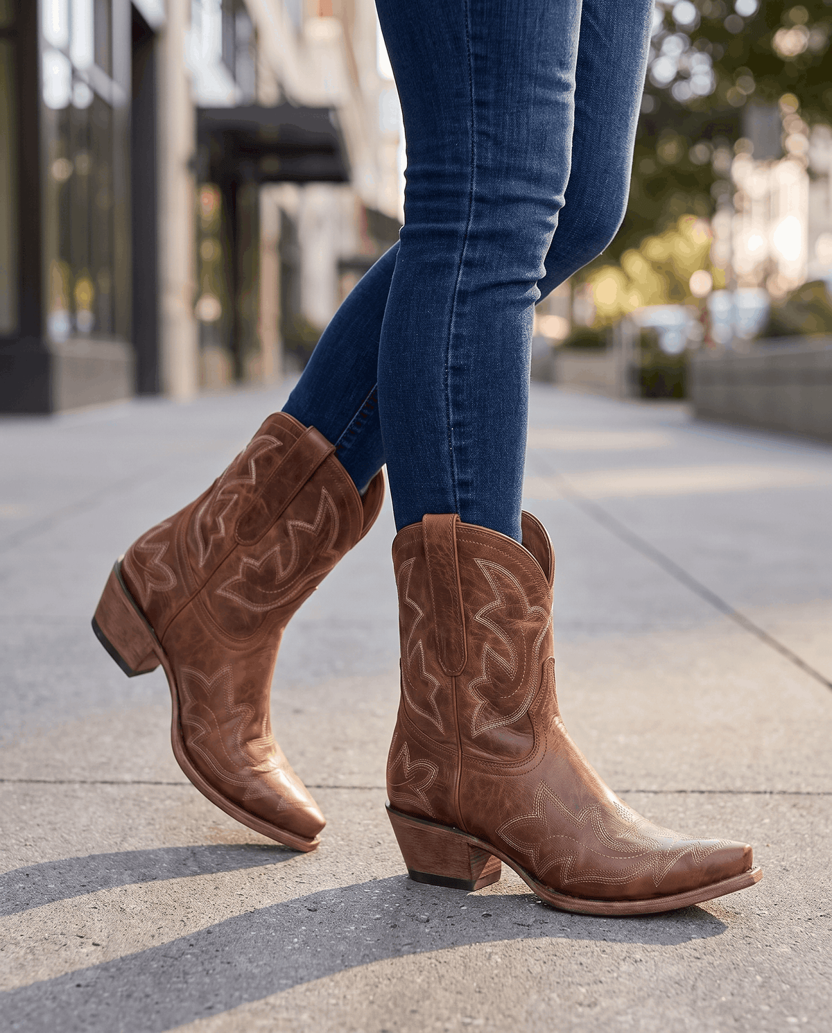 Brown embroidered boots worn walking on a sunny city sidewalk with blue jeans