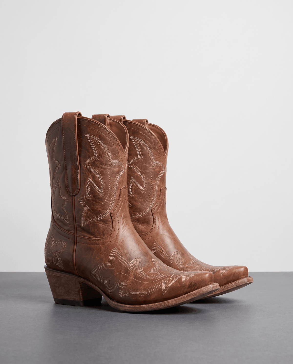 Pair of brown distressed western boots with tonal embroidery on a grey studio floor