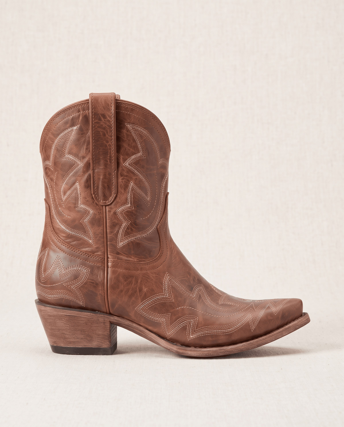 Single brown cowboy boot in side profile against a soft cream backdrop