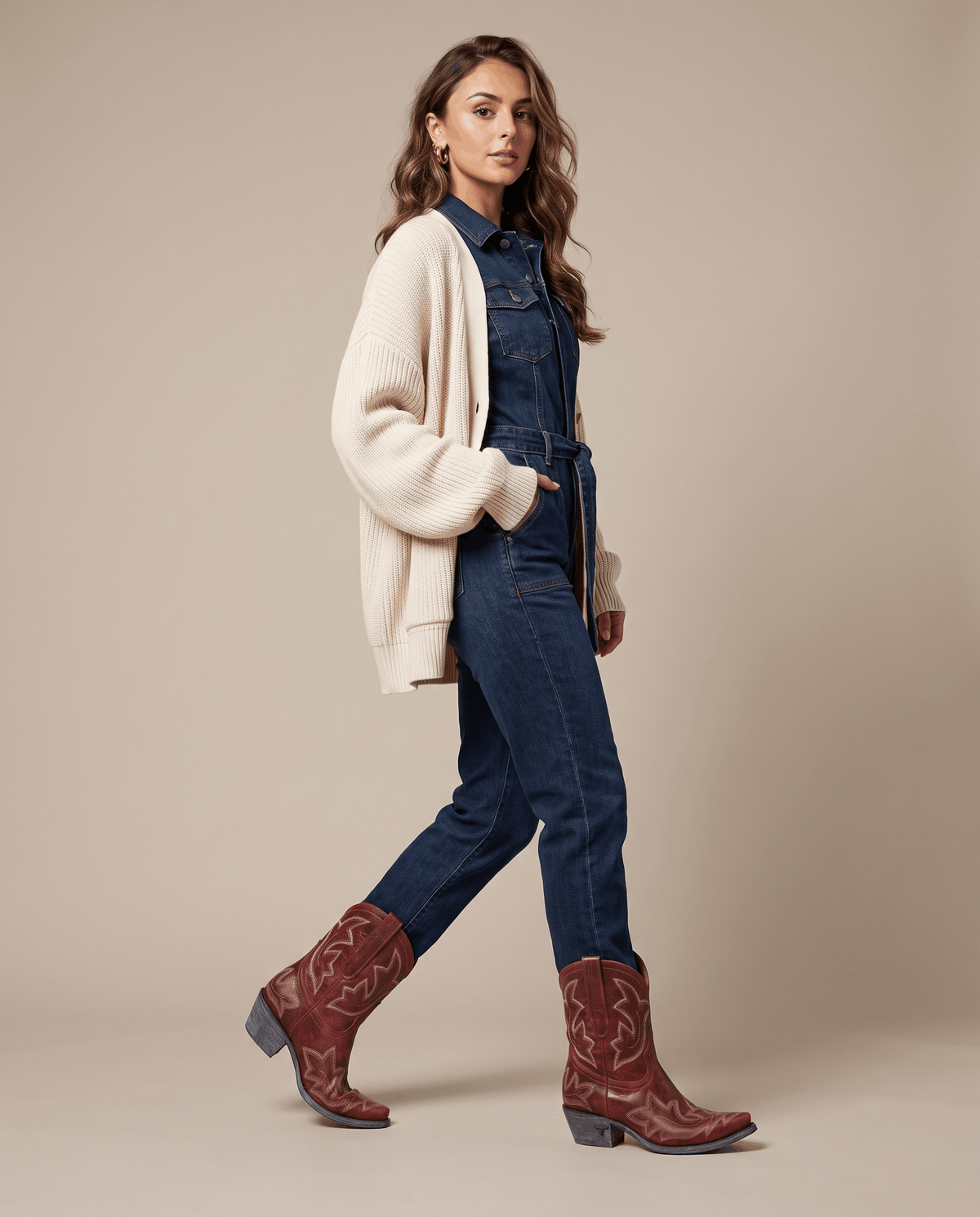 Woman in a cream cardigan and denim jumpsuit walking in red western boots