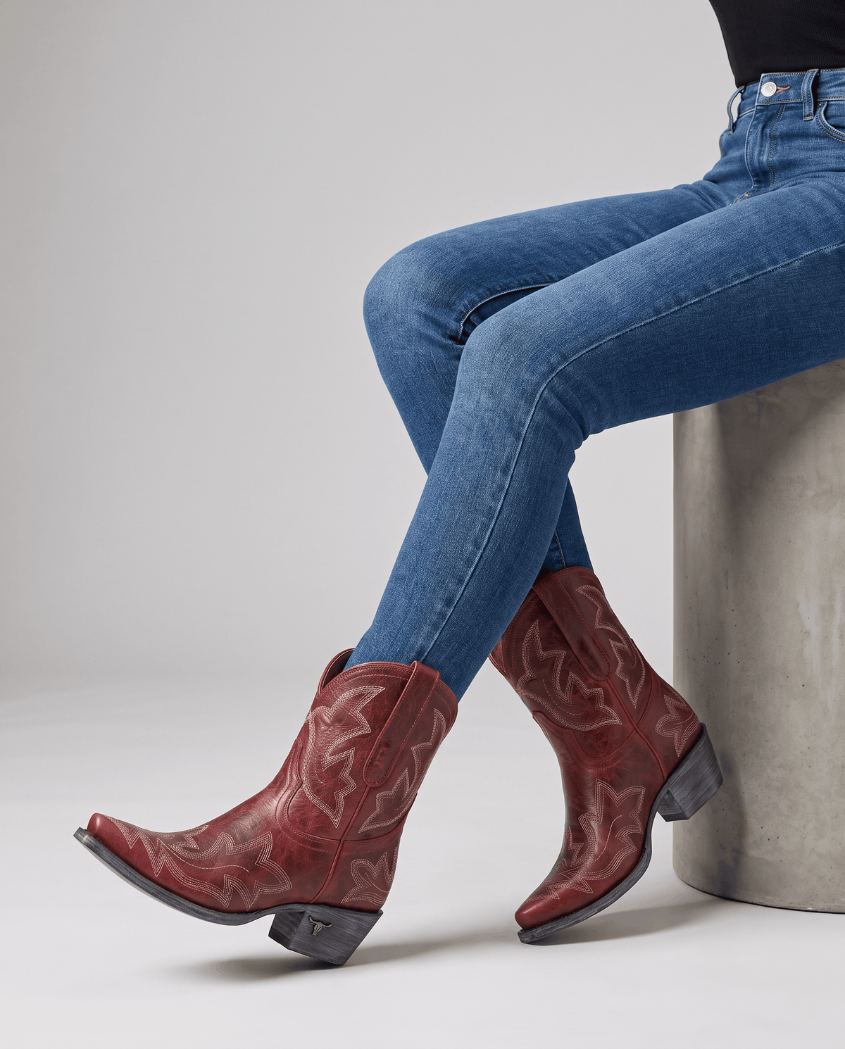 Seated model with legs crossed in red western boots and blue jeans