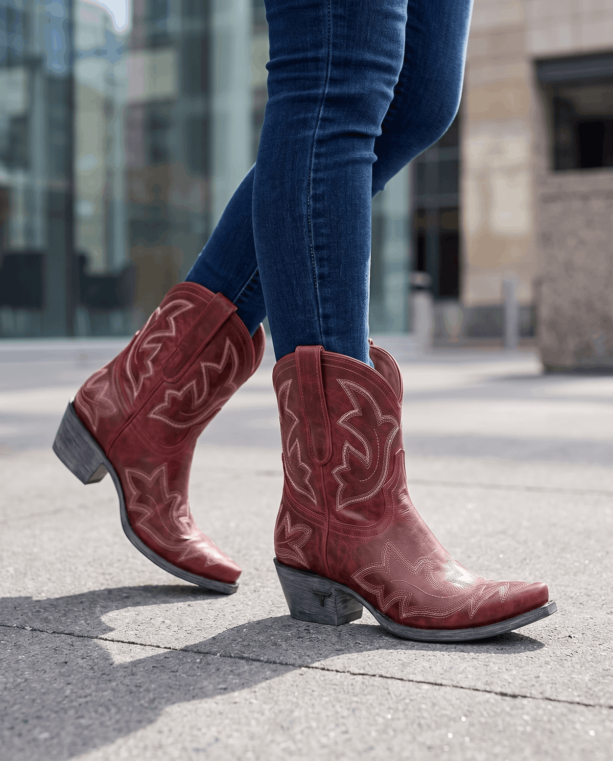 Red embroidered boots worn walking on a city street with tucked blue jeans