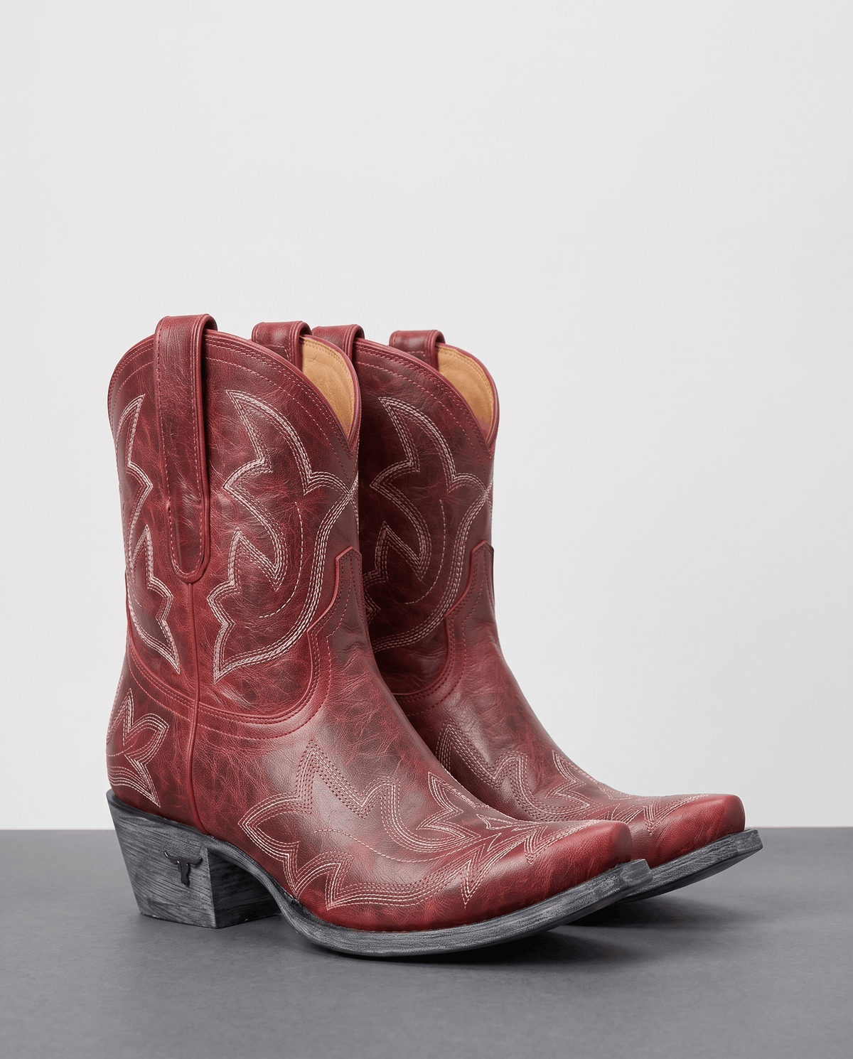 Pair of red embroidered short cowboy boots on a grey studio floor