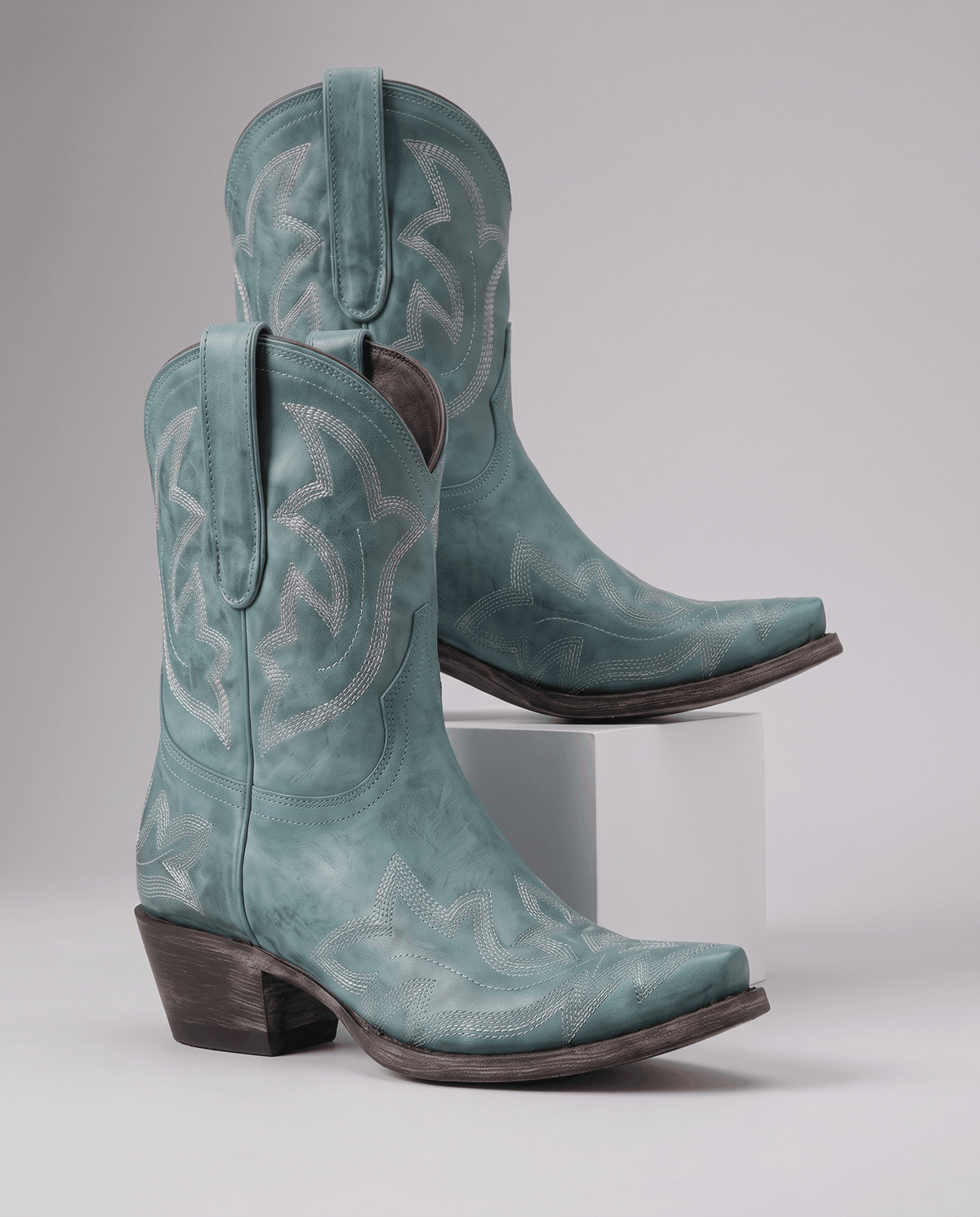 Pair of teal snip-toe short cowboy boots with tonal embroidery displayed on a pedestal