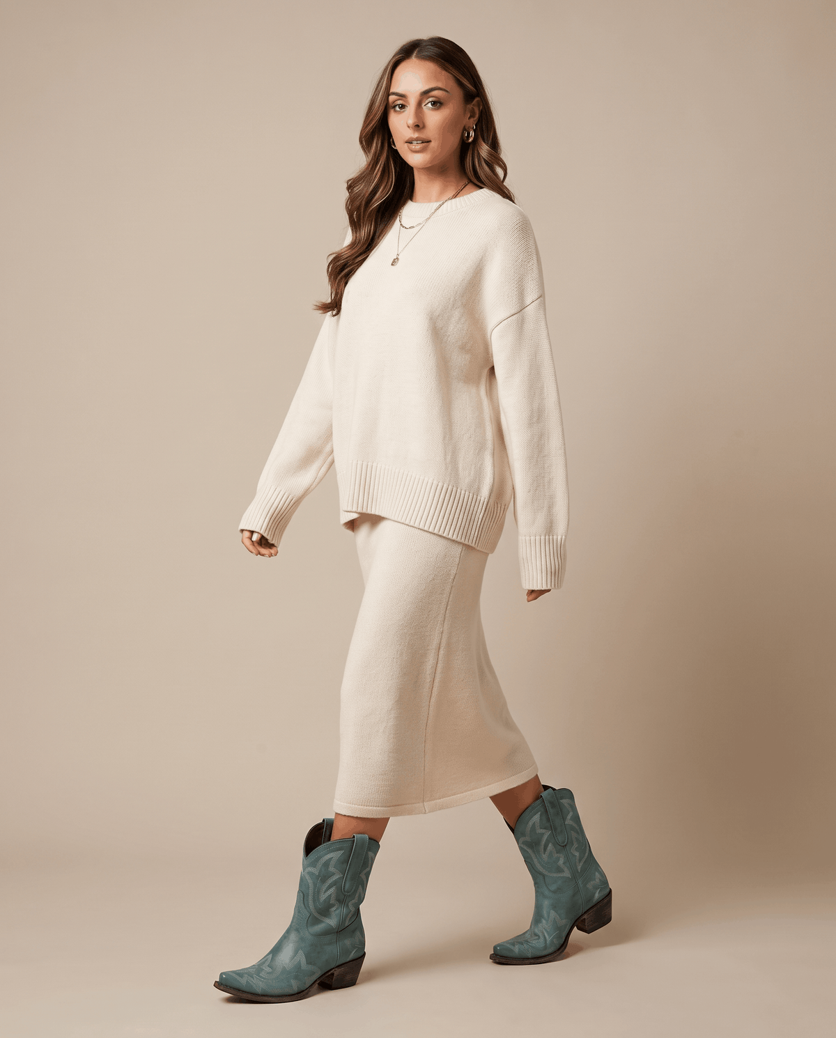 Woman in a cream sweater and knit midi skirt walking in teal cowboy boots